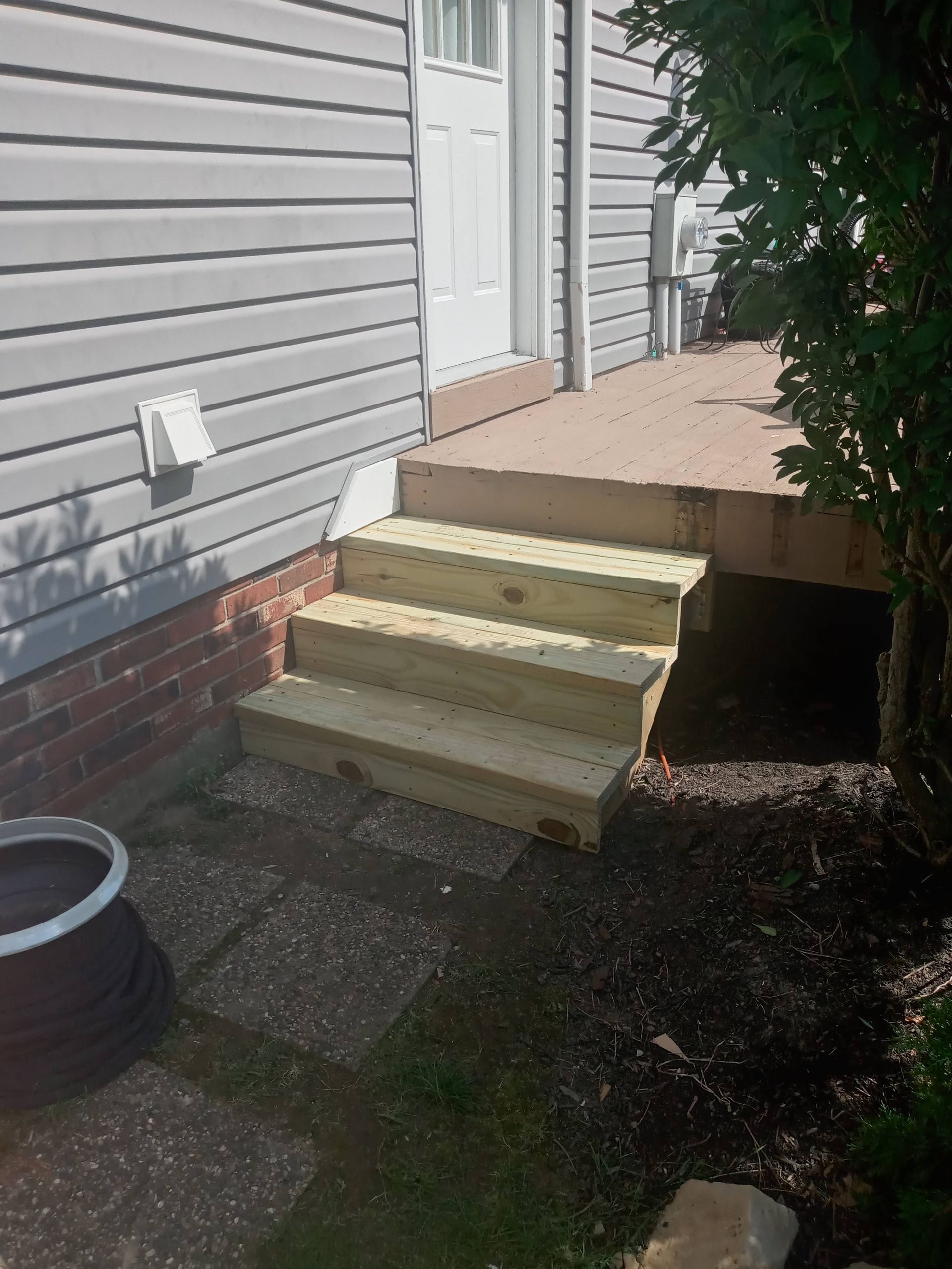 Wooden steps leading to a deck and white door on a house with gray siding.