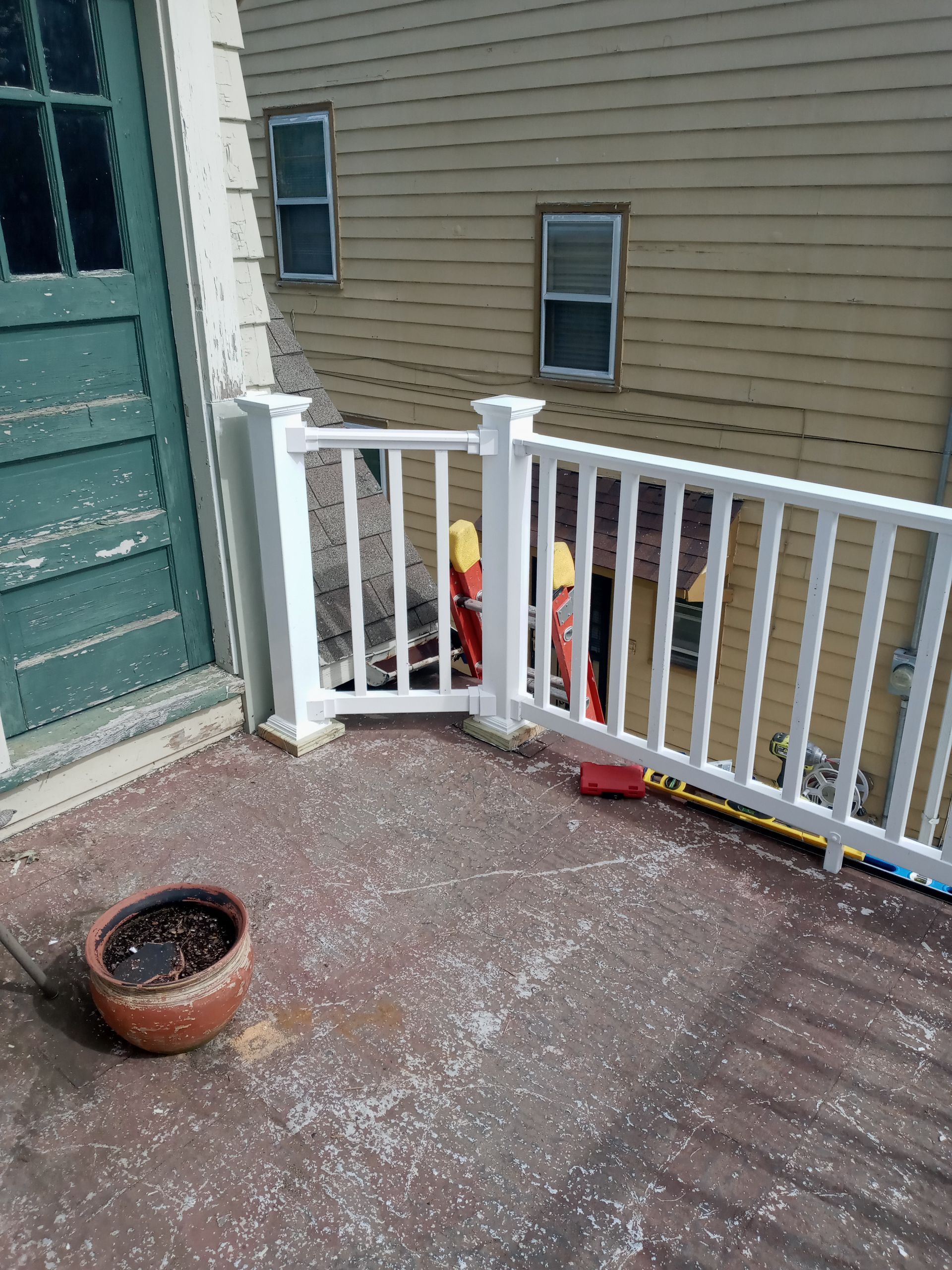 Deck with white railing, weathered wood flooring, potted plant, and peeling paint on a nearby green door.