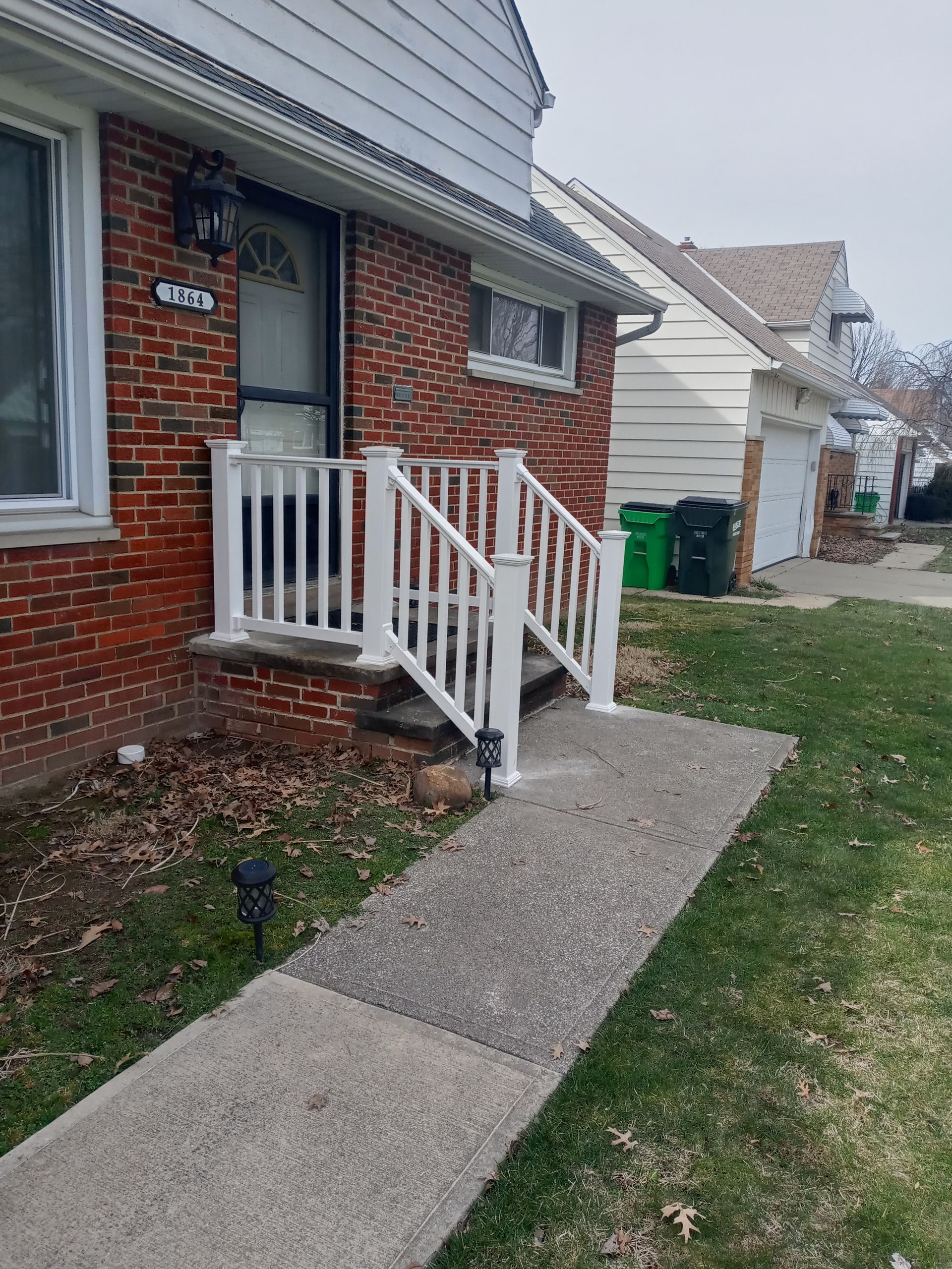 White railing on a brick house porch. A sidewalk leads up to the front door.
