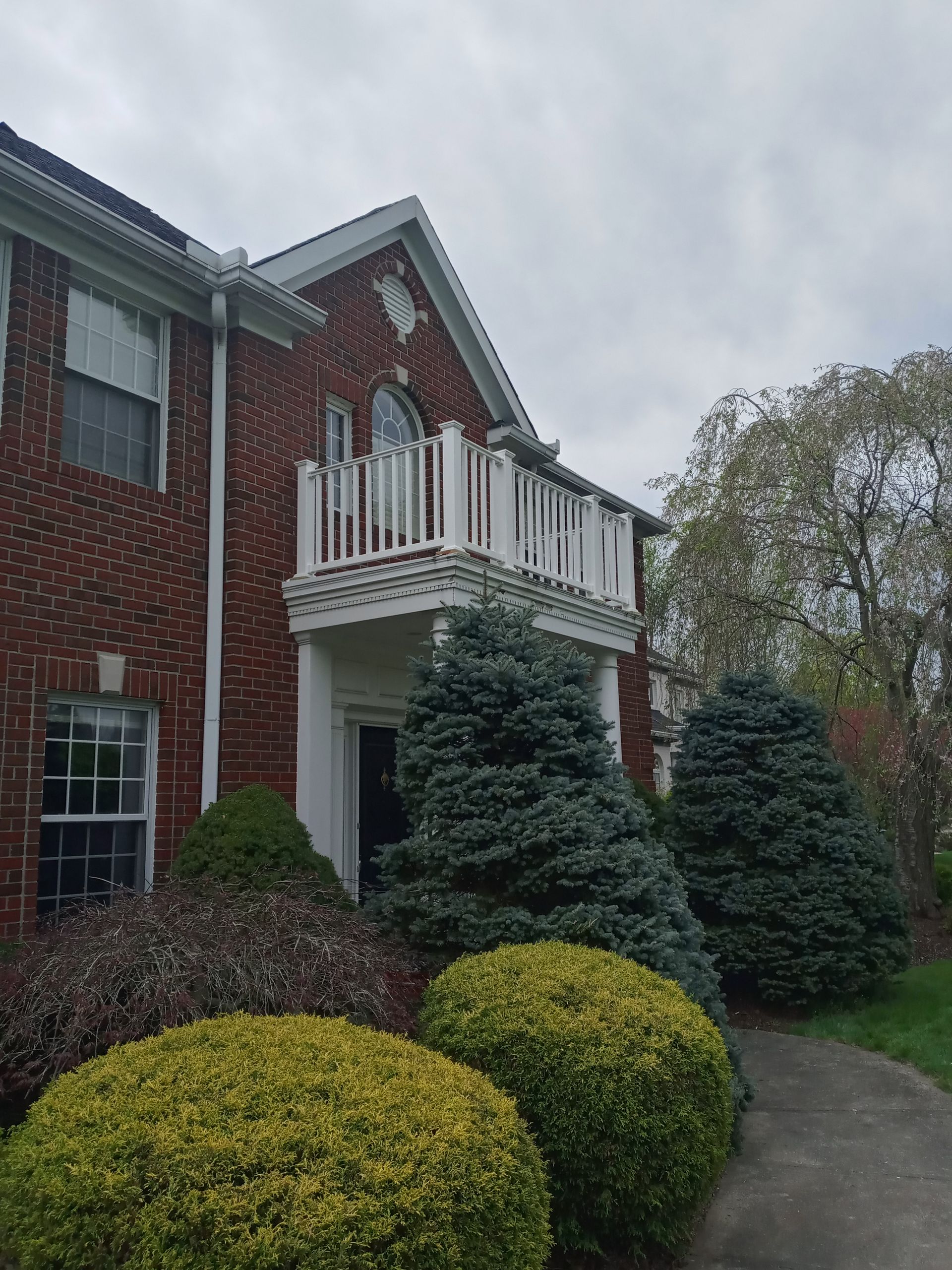 Brick building with white balcony and trim, lush bushes and a pathway.
