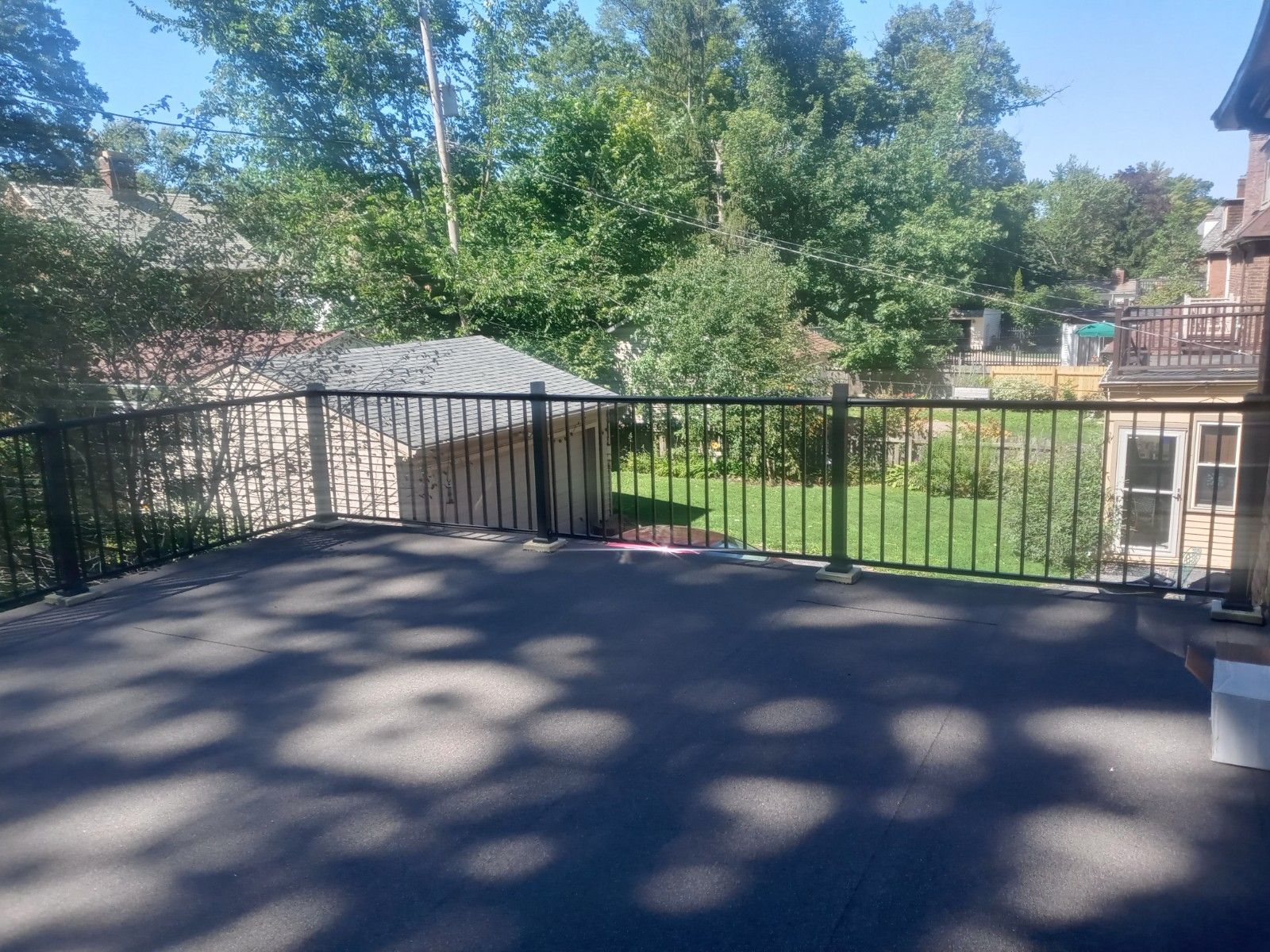 Black fenced deck overlooking a backyard with trees and a shed on a sunny day.