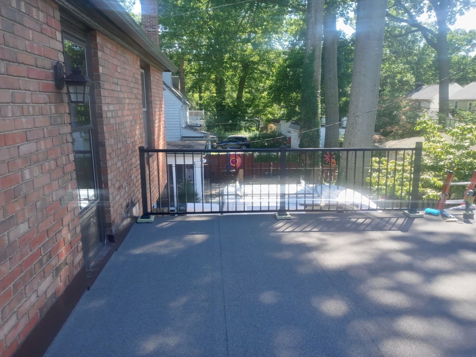 Black railing on flat roof next to a brick building; trees in background.