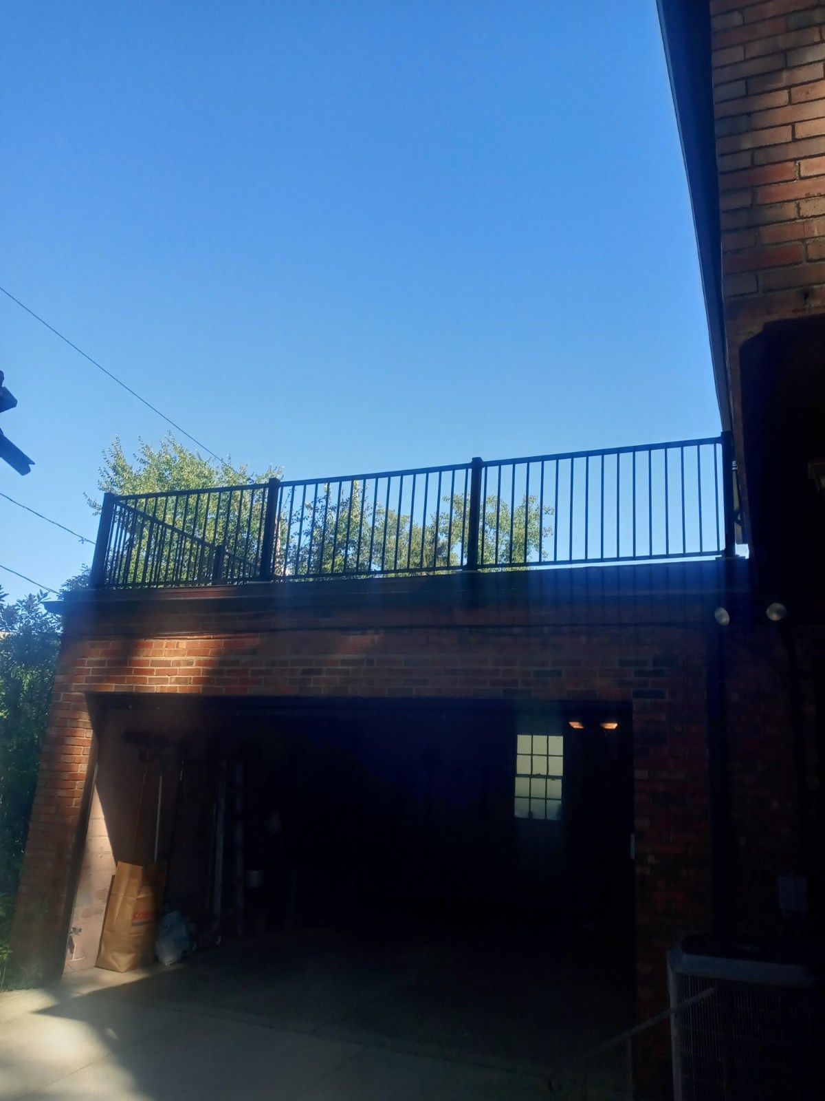 Brick building with a garage below a balcony with black railings against a blue sky.