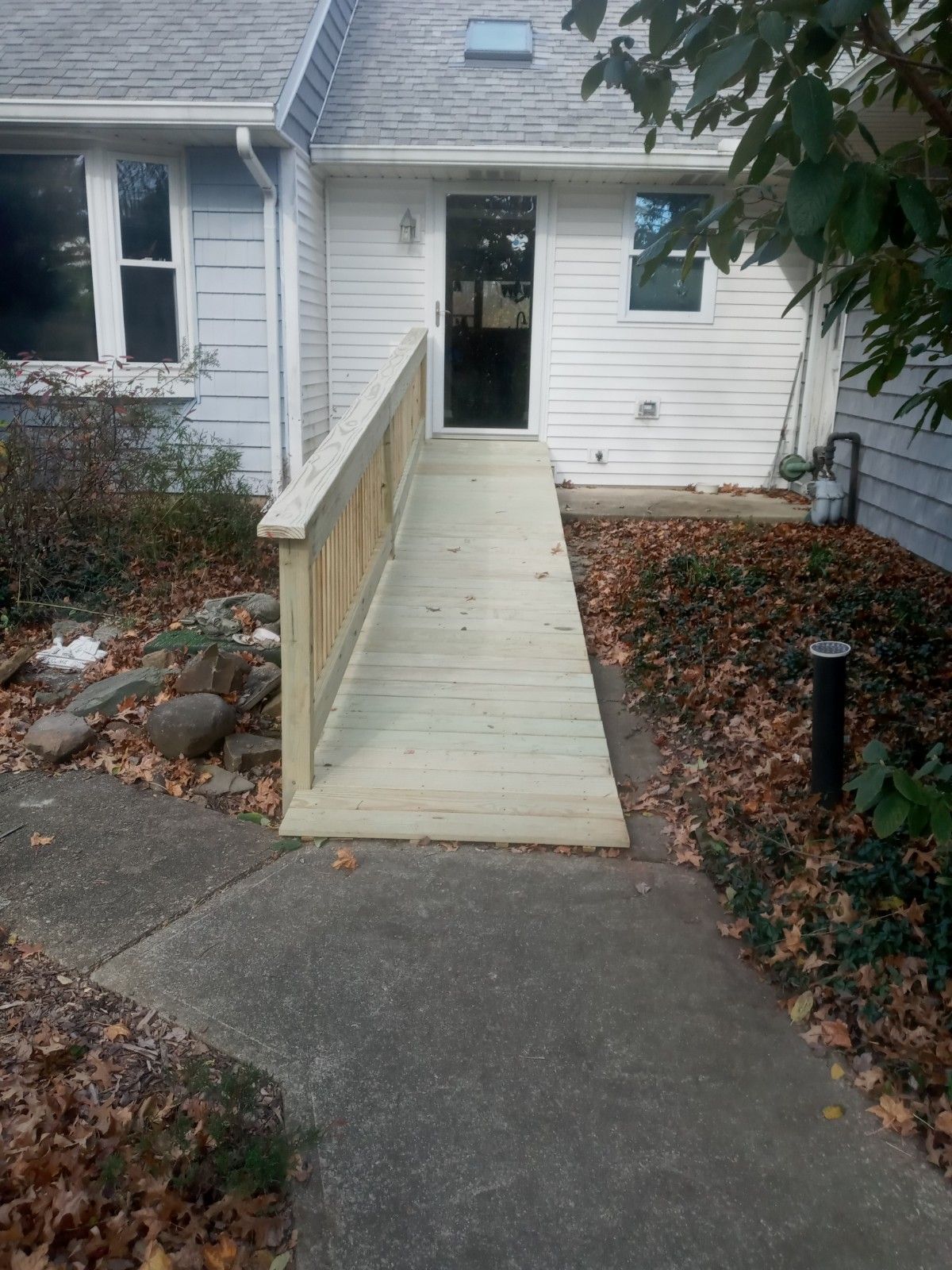 Exterior view of a building with a wooden ramp leading to the entrance door, surrounded by foliage.