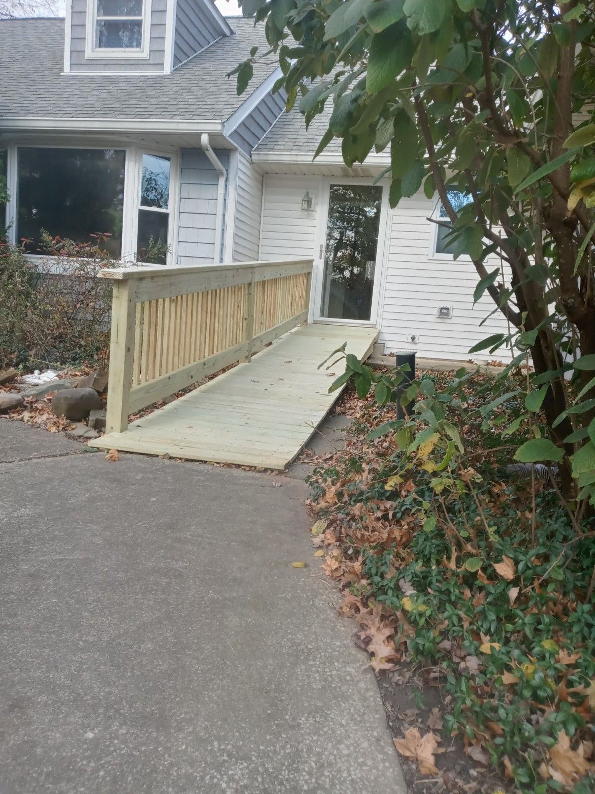 Wooden ramp leading to a doorway of a white house. Side of the house has white siding.