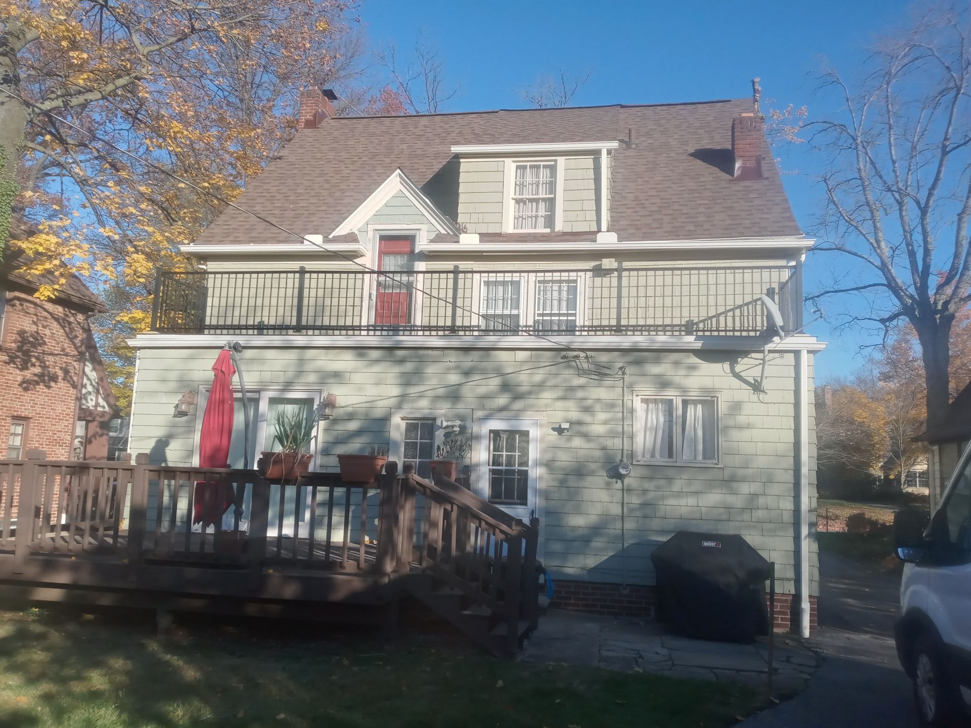 Two-story house with green siding, a deck, and an umbrella, under a blue sky.