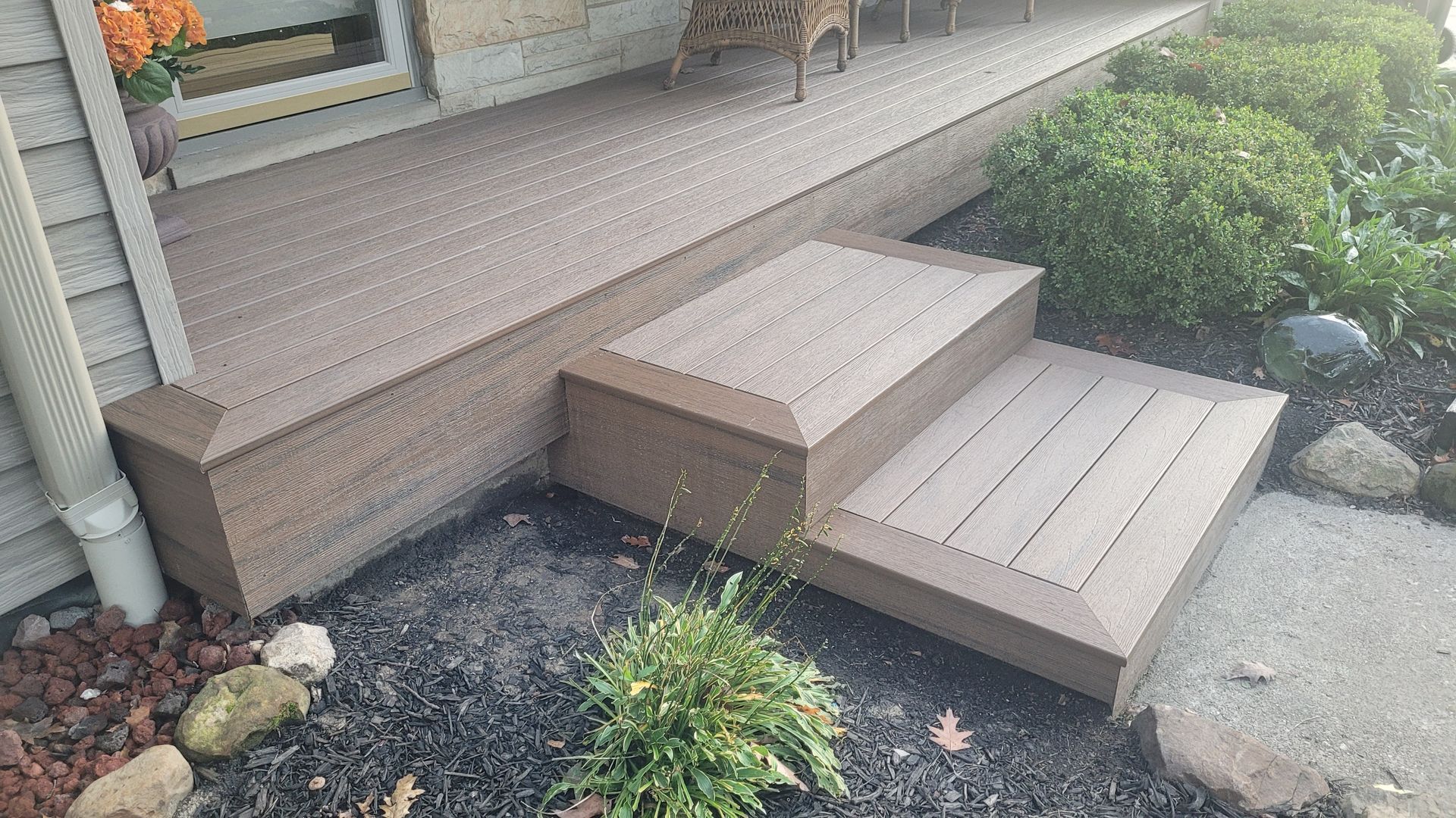 Composite deck with two steps leading to a porch next to shrubbery and a walkway.