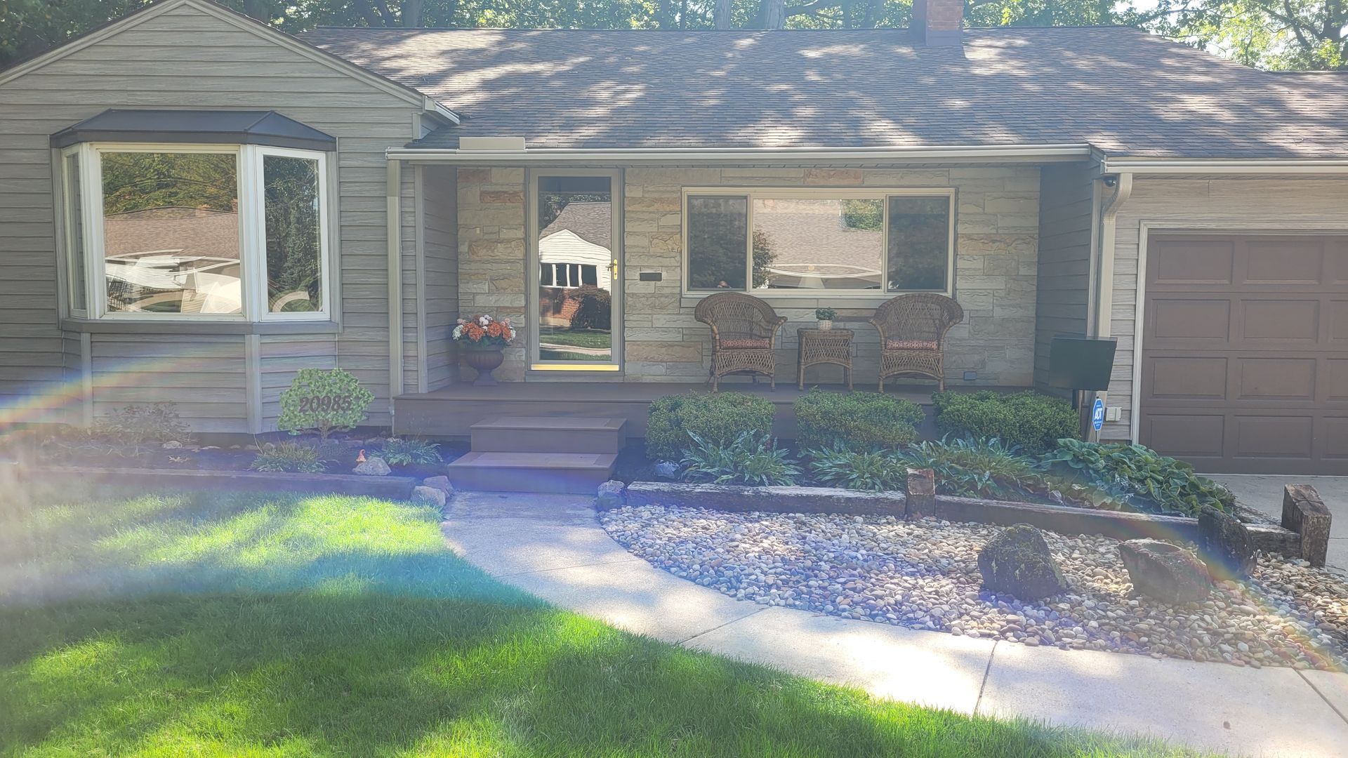 A gray house with a small front porch, flanked by flower beds and a green lawn.