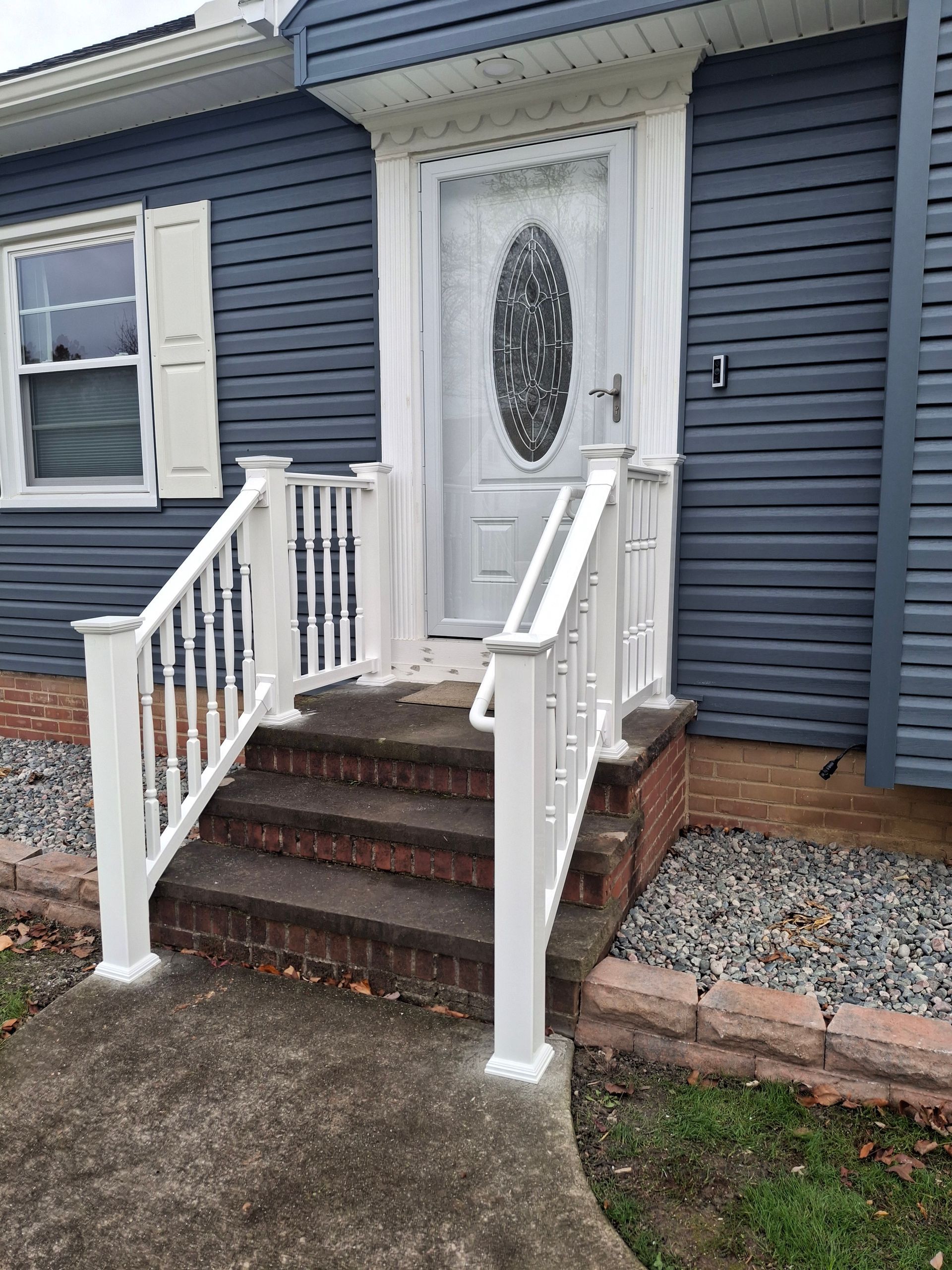 White-railed steps leading to a front door with a decorative oval window, blue siding, and white shutters.