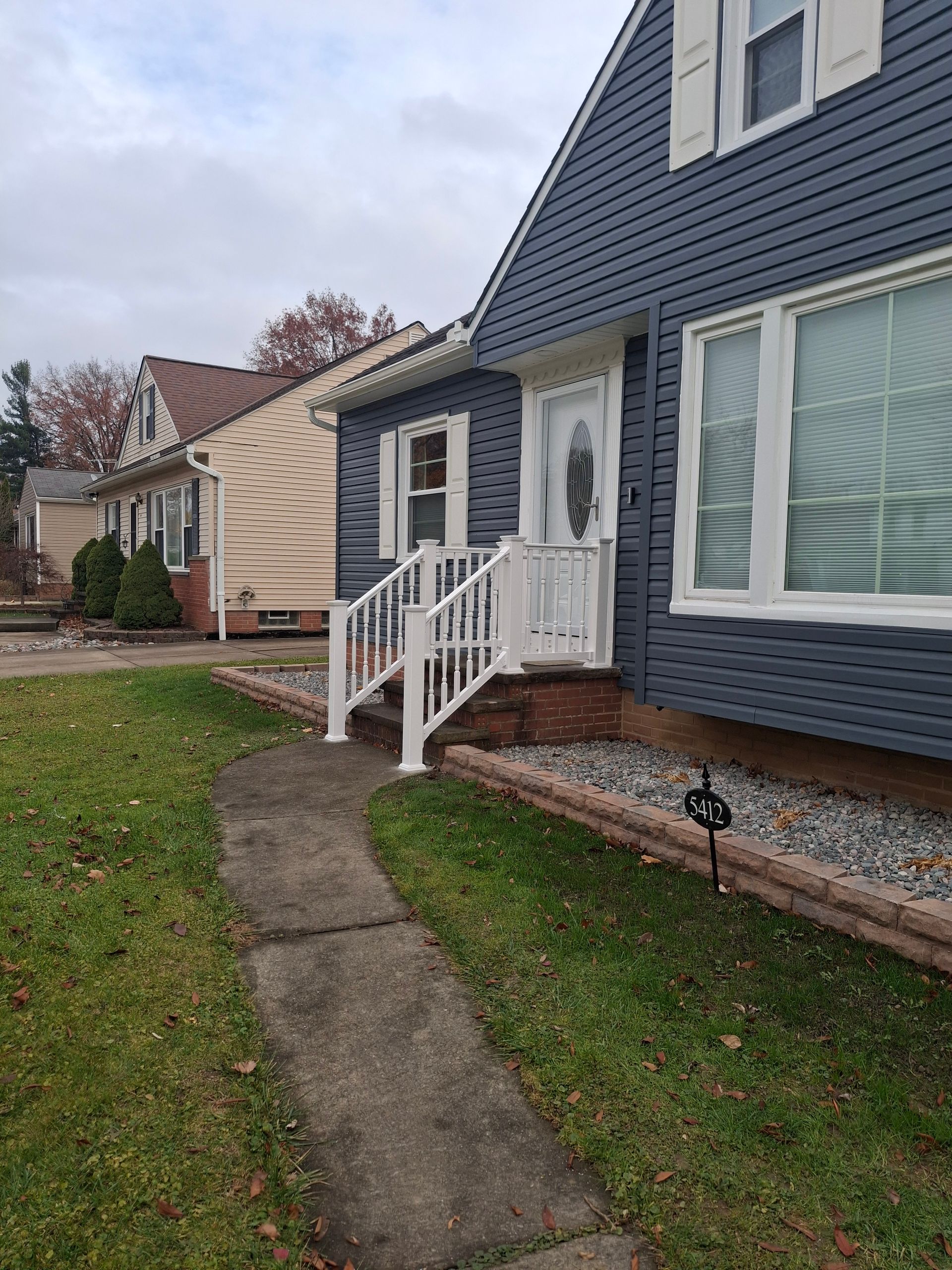 Blue house with white trim, front porch, and walkway, in a neighborhood with overcast sky.