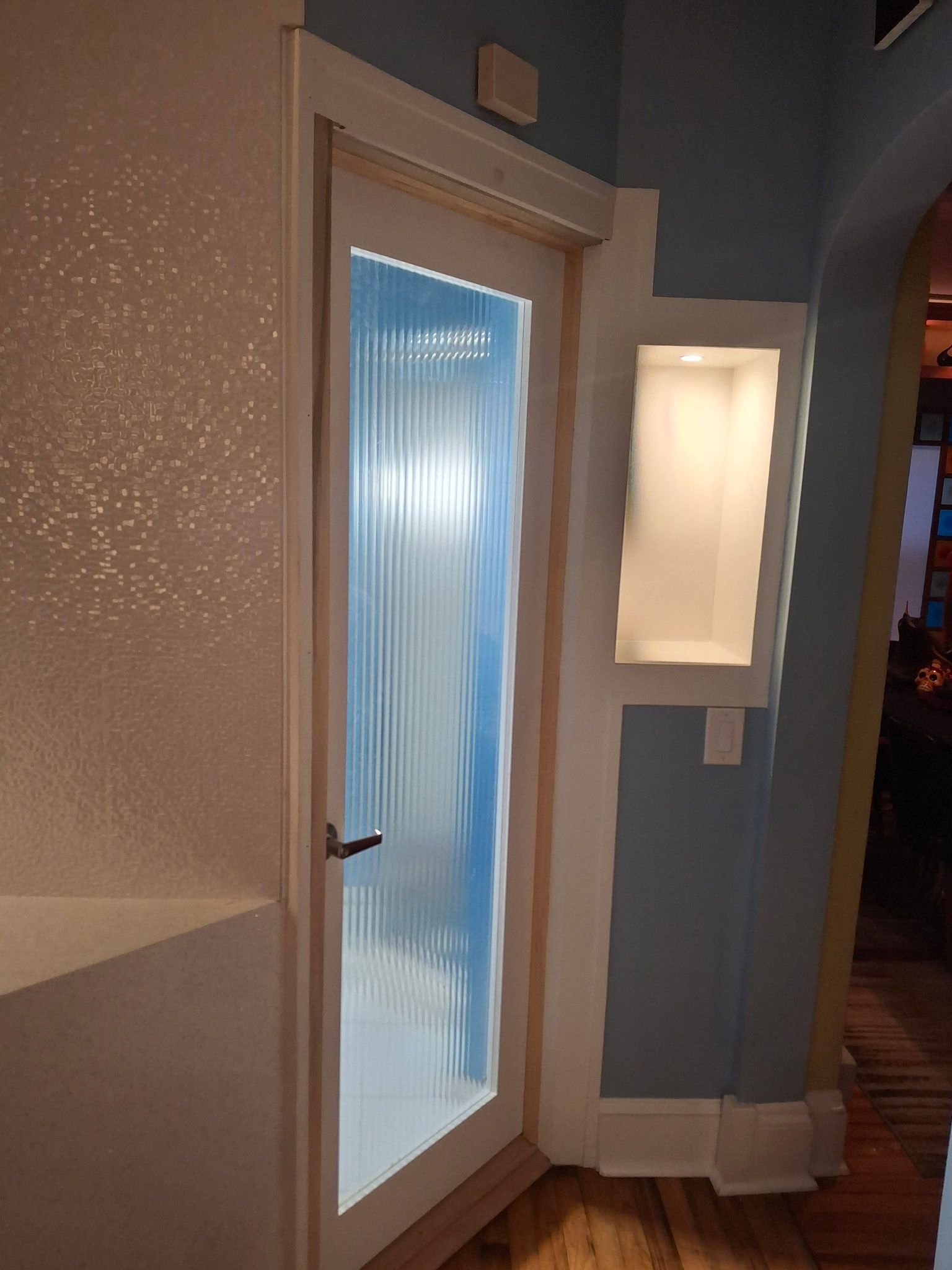 A white door with ribbed glass, next to a recessed wall niche on a blue wall.