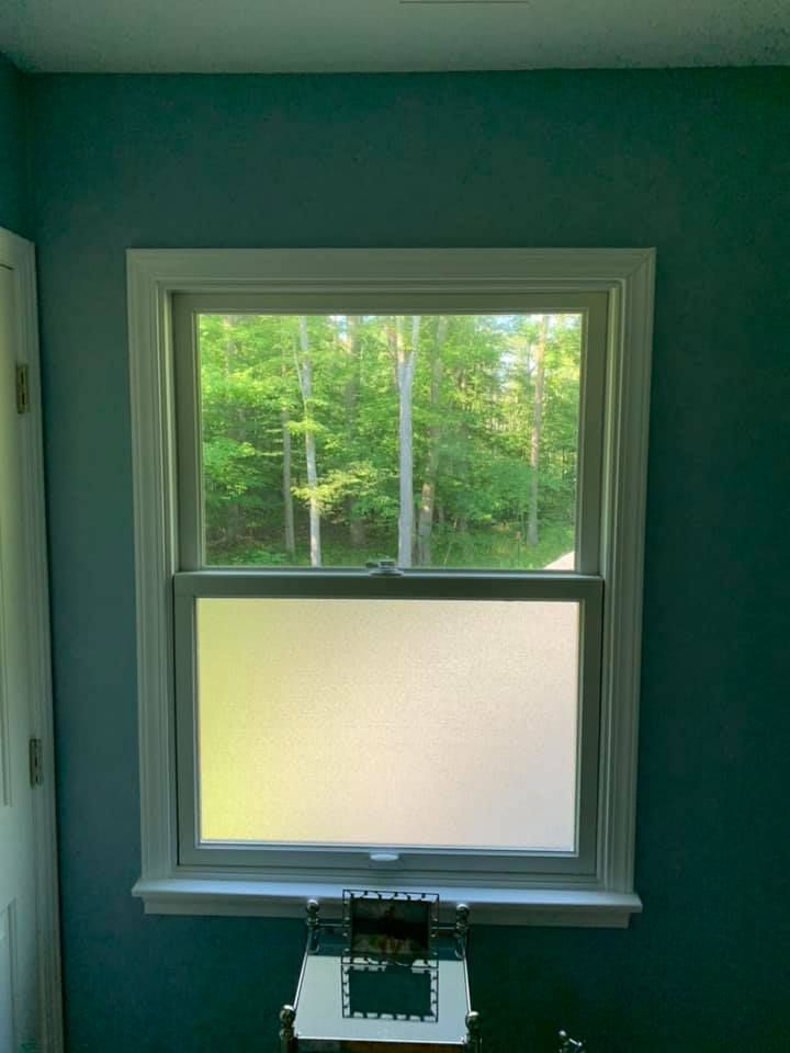 Window with frosted lower pane, white trim, turquoise wall, looking out at green trees.