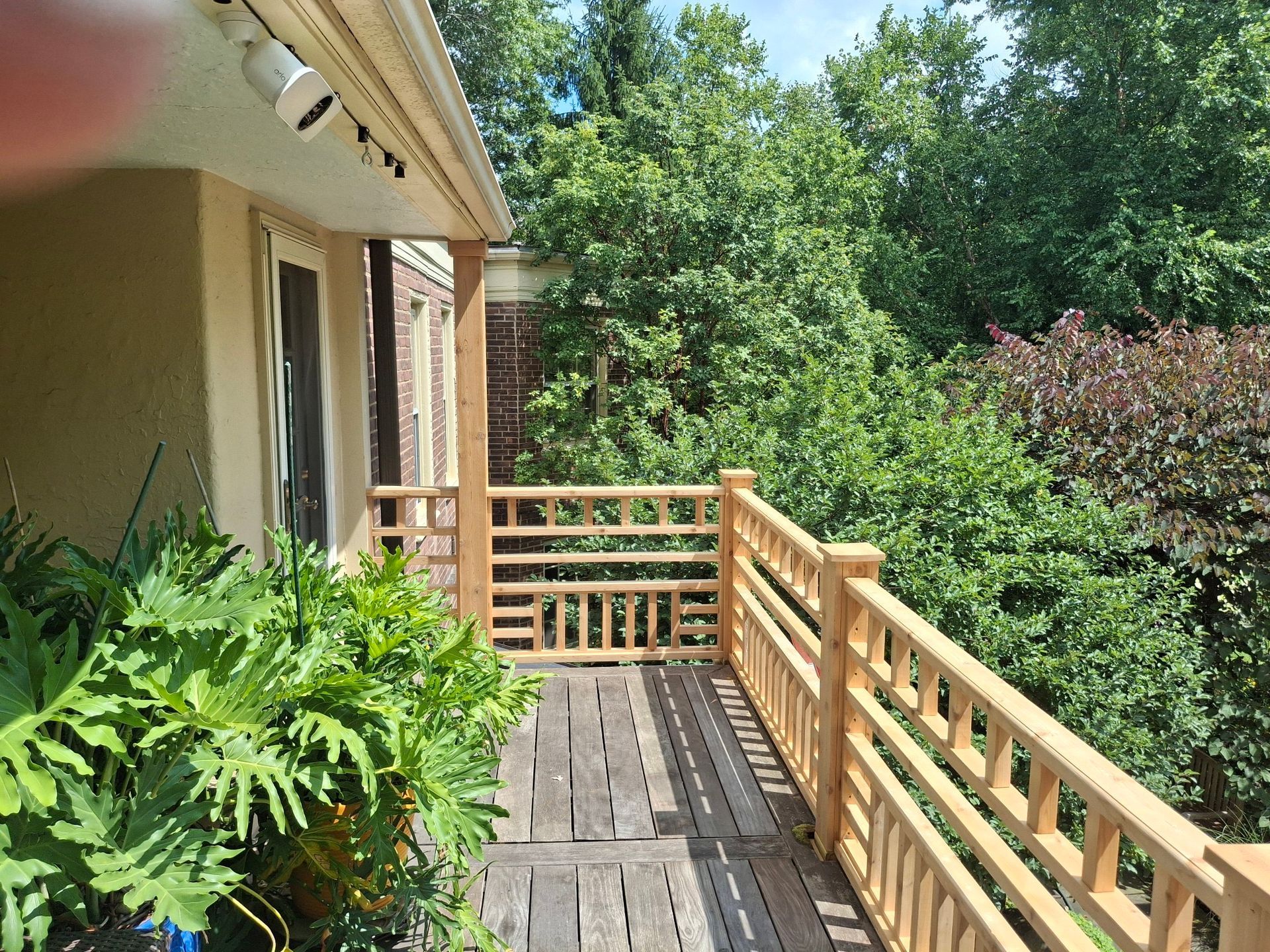 Wooden deck with railing overlooking lush green trees.