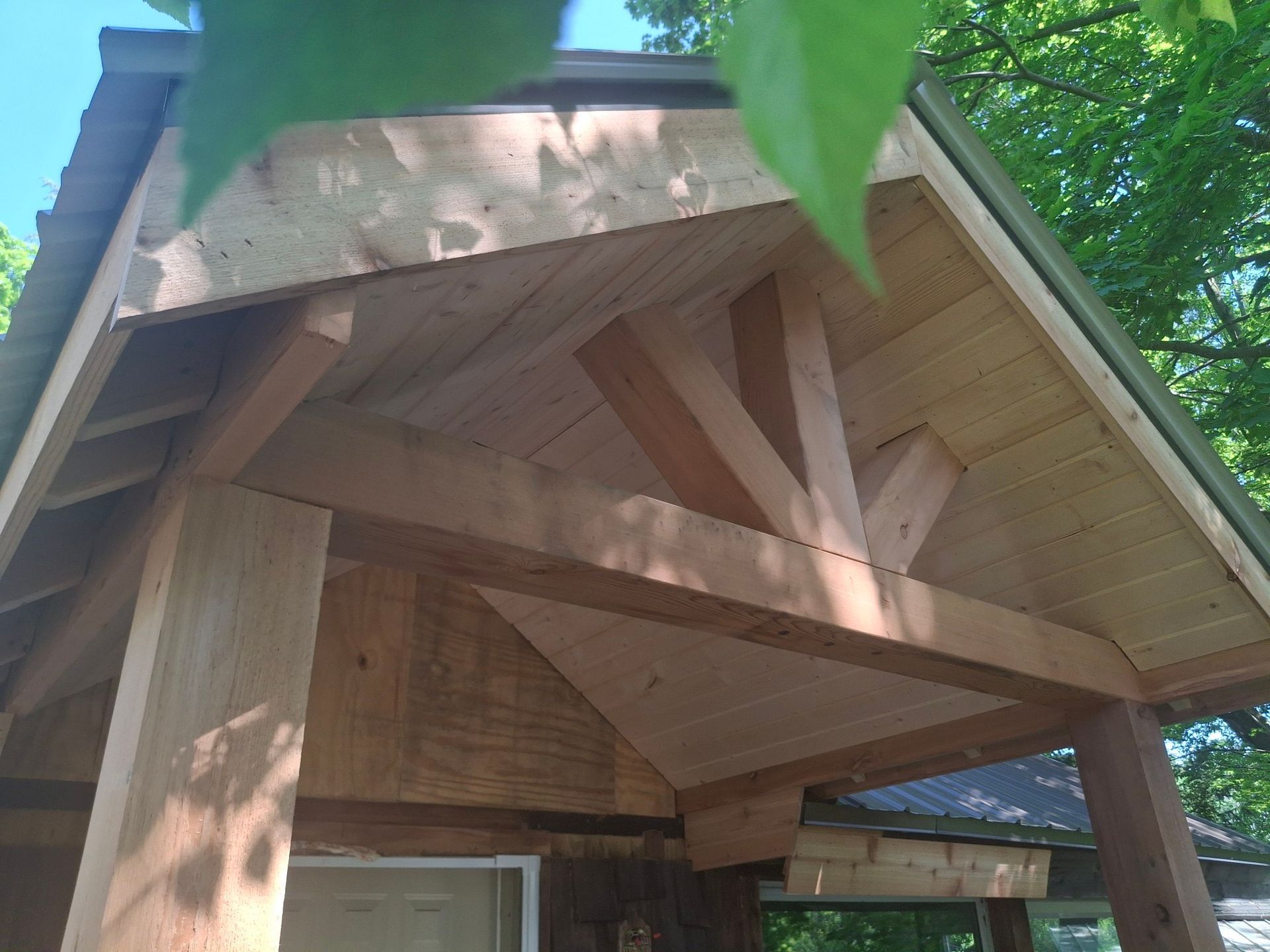 Wooden porch roof with beams and siding, seen from below, against a blue sky.
