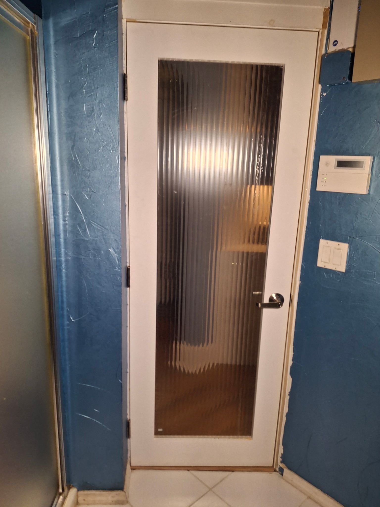 White door with vertical, textured glass panel in a blue-walled bathroom.