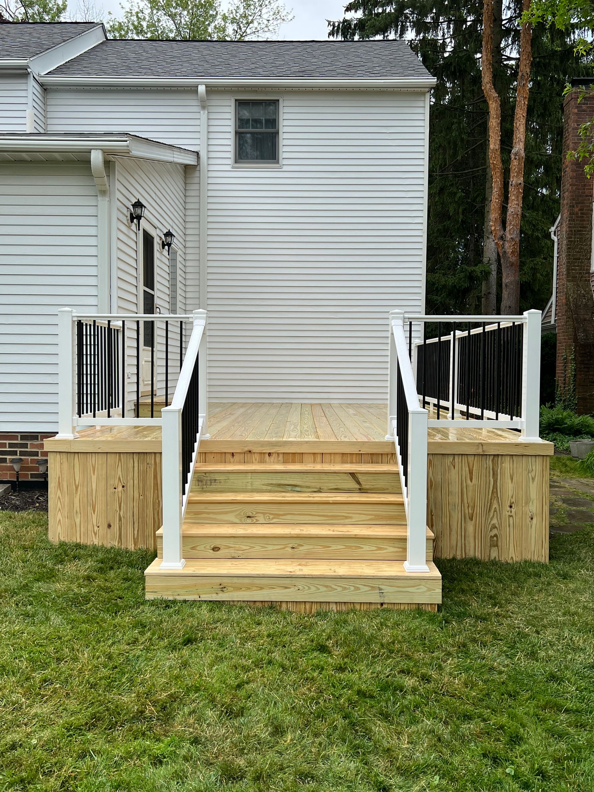 Wooden deck with steps leading up to a white, corrugated-sided building. Black railings and white posts.