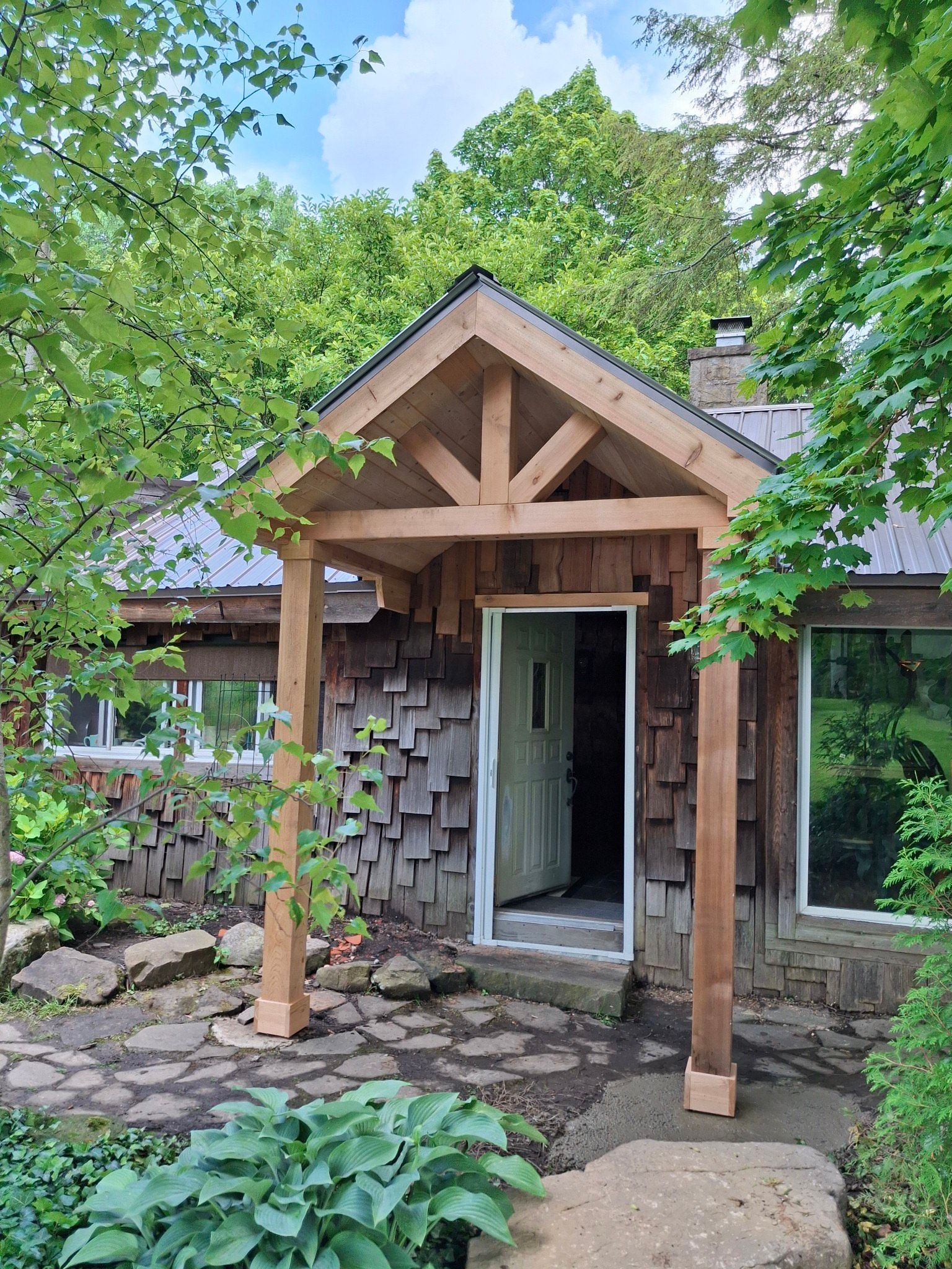 Rustic cabin exterior with a wooden porch and open door surrounded by greenery.