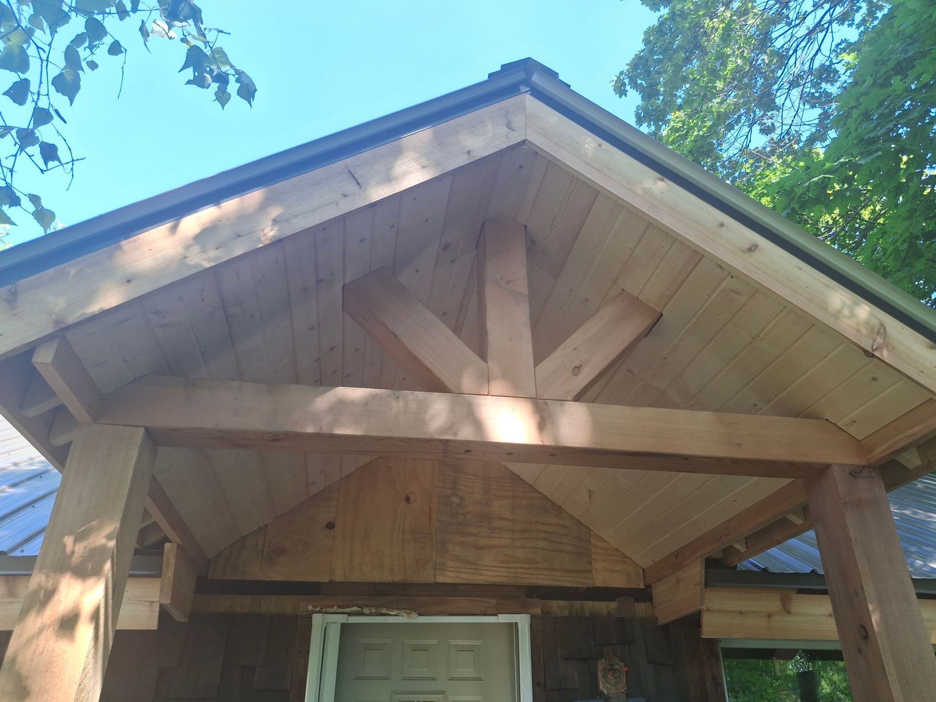 Wooden porch roof with a support beam structure, over a building's entrance, sunny day.