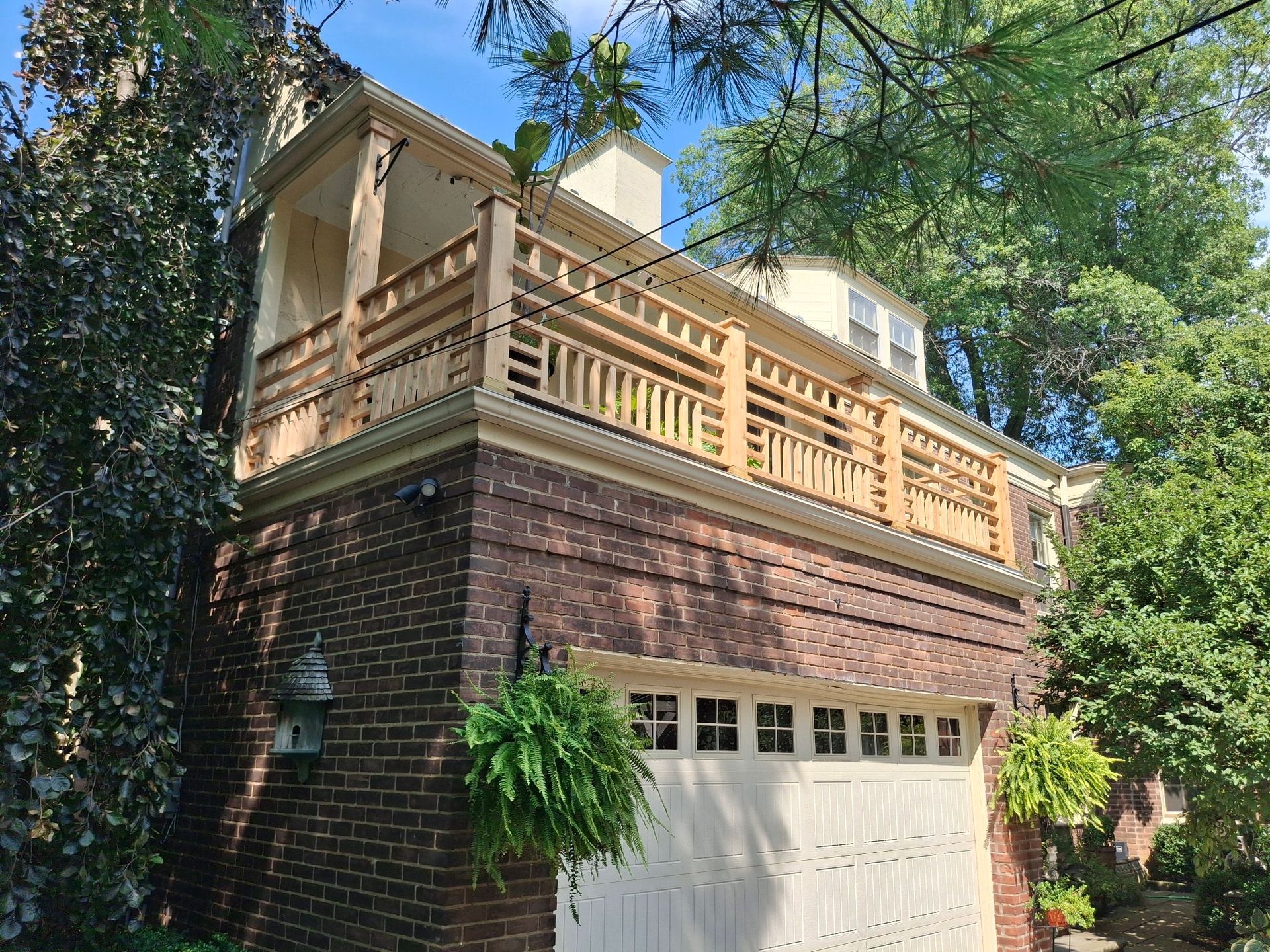 Brick garage with wooden balcony. Green ferns hang from the brick. Trees frame the view.