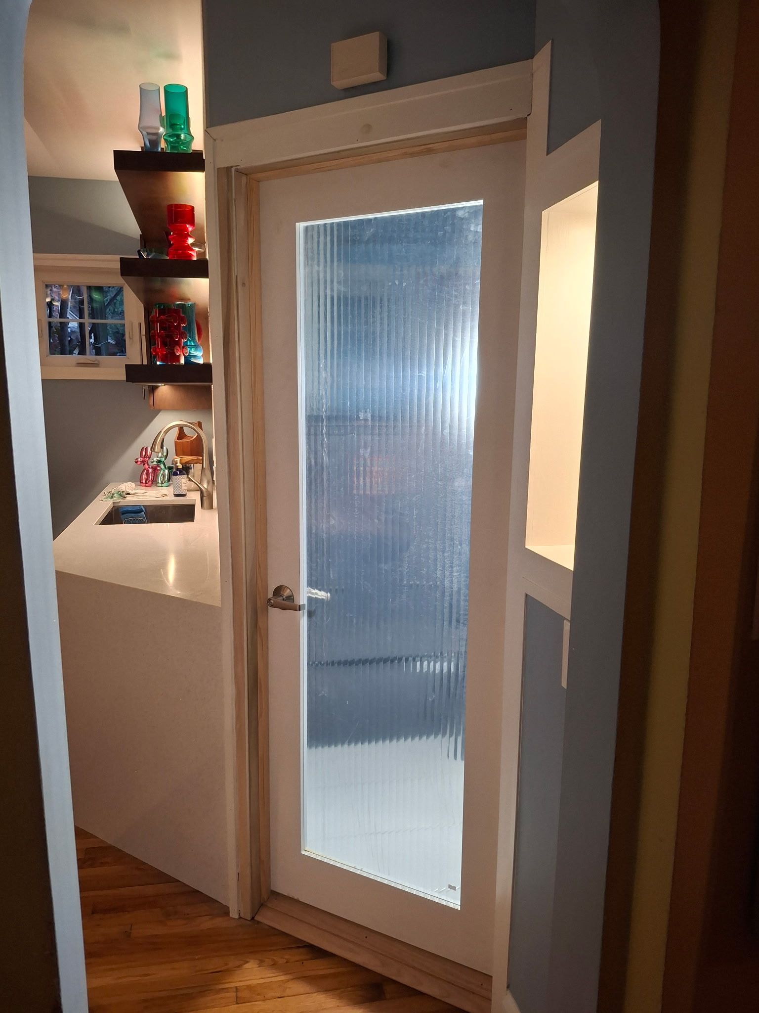White framed door with textured glass, leading to a small kitchen area.