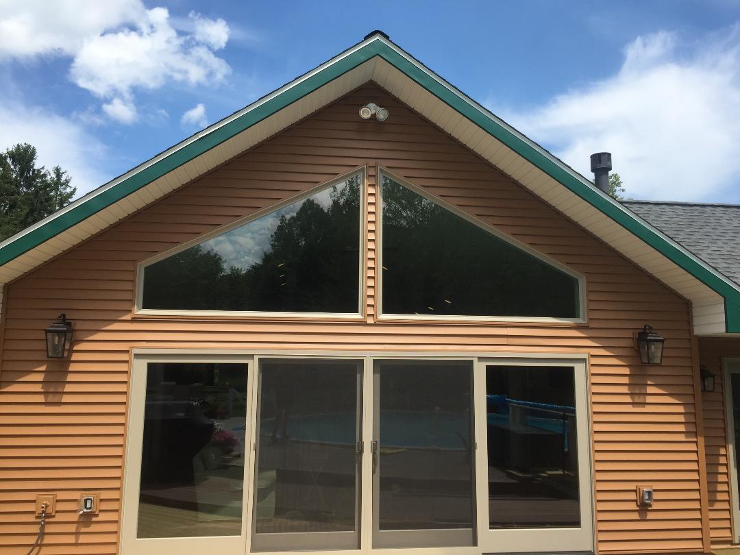 Tan house with triangle window above sliding glass doors, blue sky background.