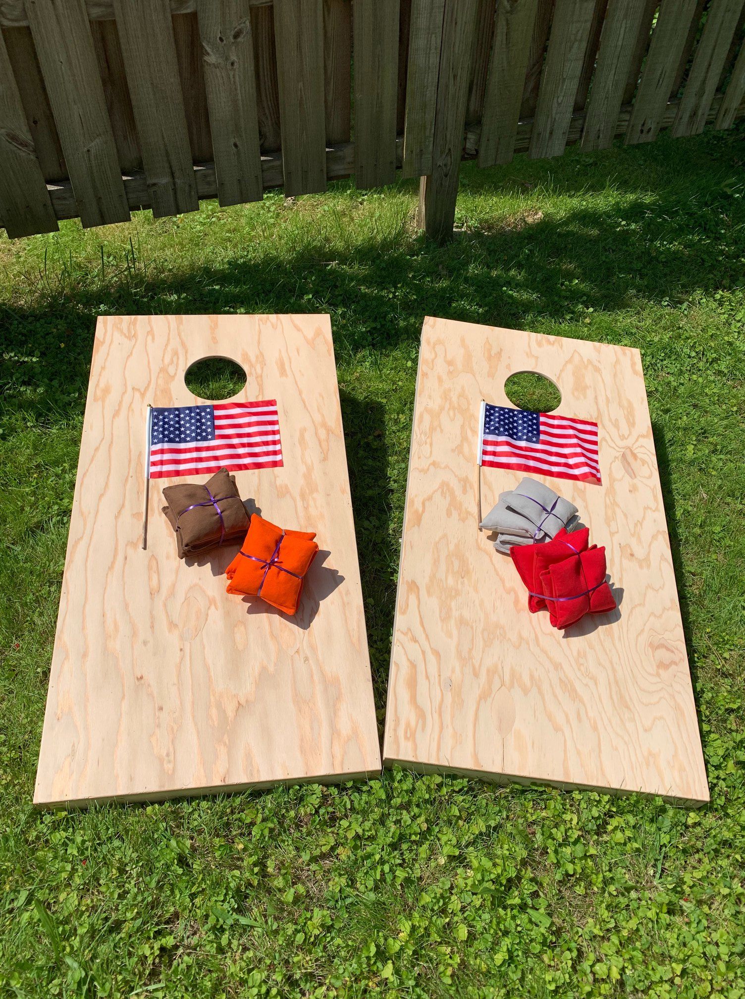 Two wooden cornhole boards with bean bags and American flags on grass.