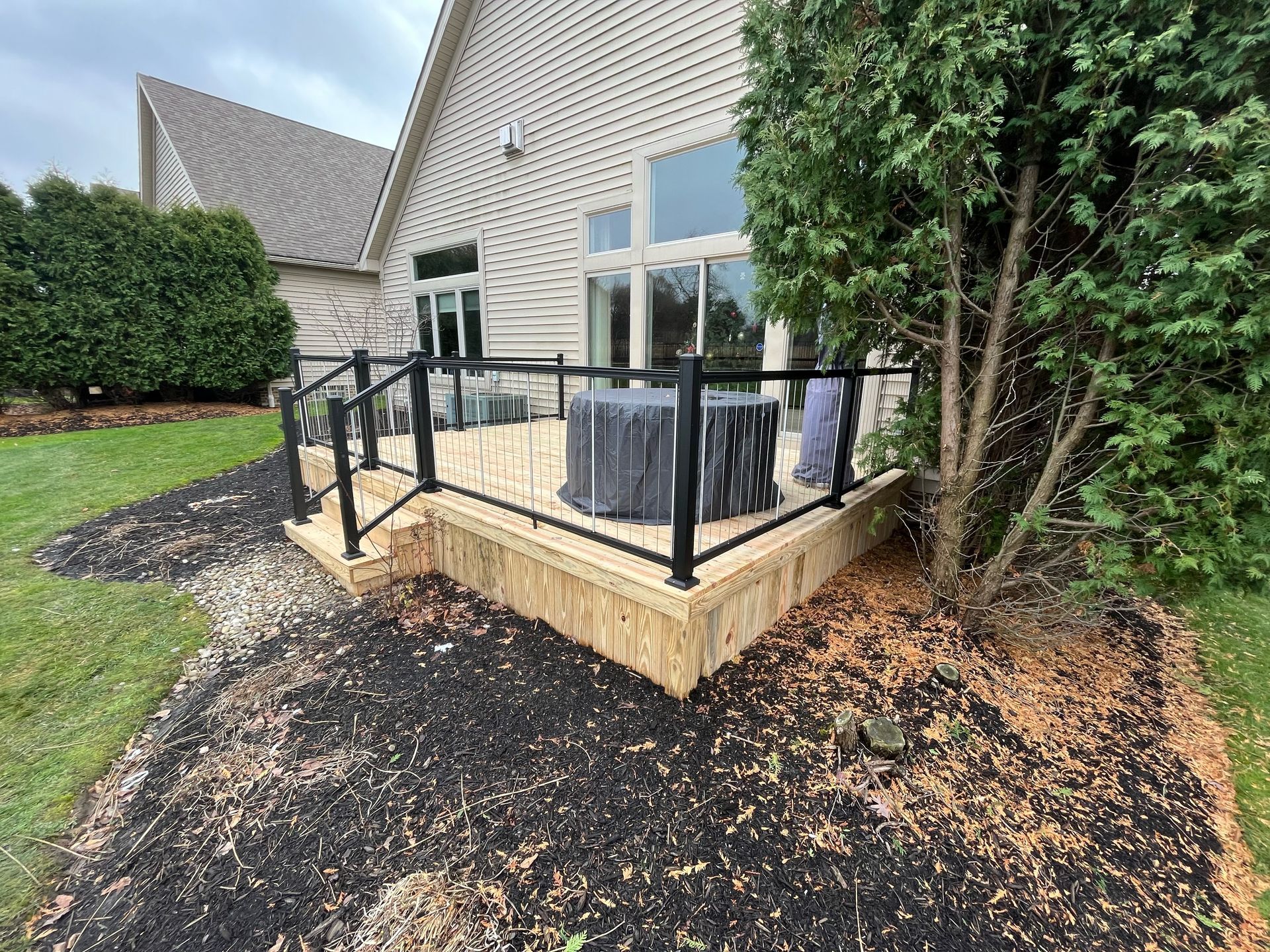 Black railing surrounds a patio with a table. Dark mulch, and landscaping border the patio.