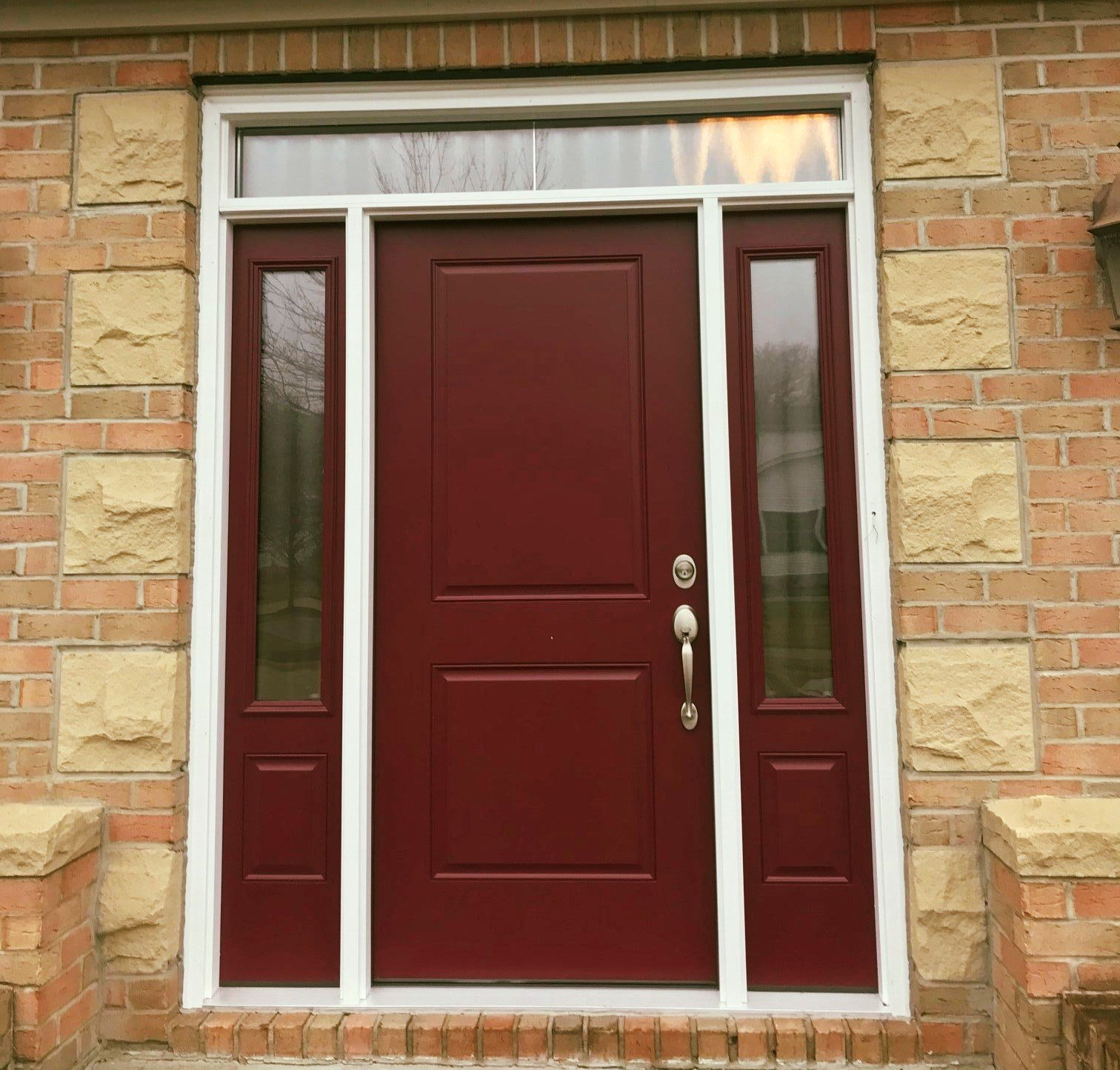 Burgundy front door with sidelights, white trim, on brick building.