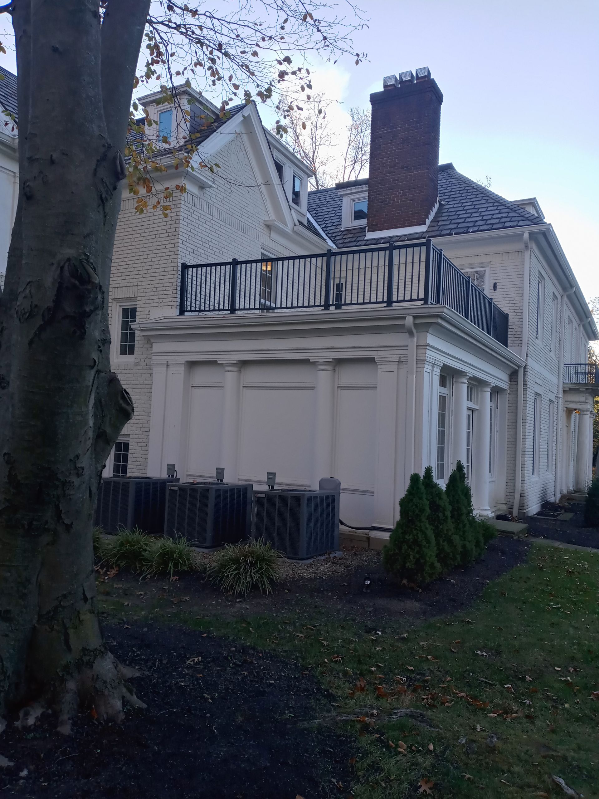 White building with black railing, chimney, and air conditioning units on a lawn.