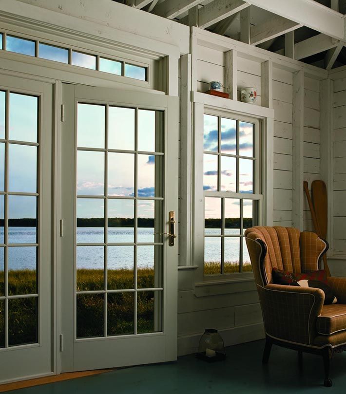 White-walled room with French doors and window overlooking a body of water; armchair sits inside.