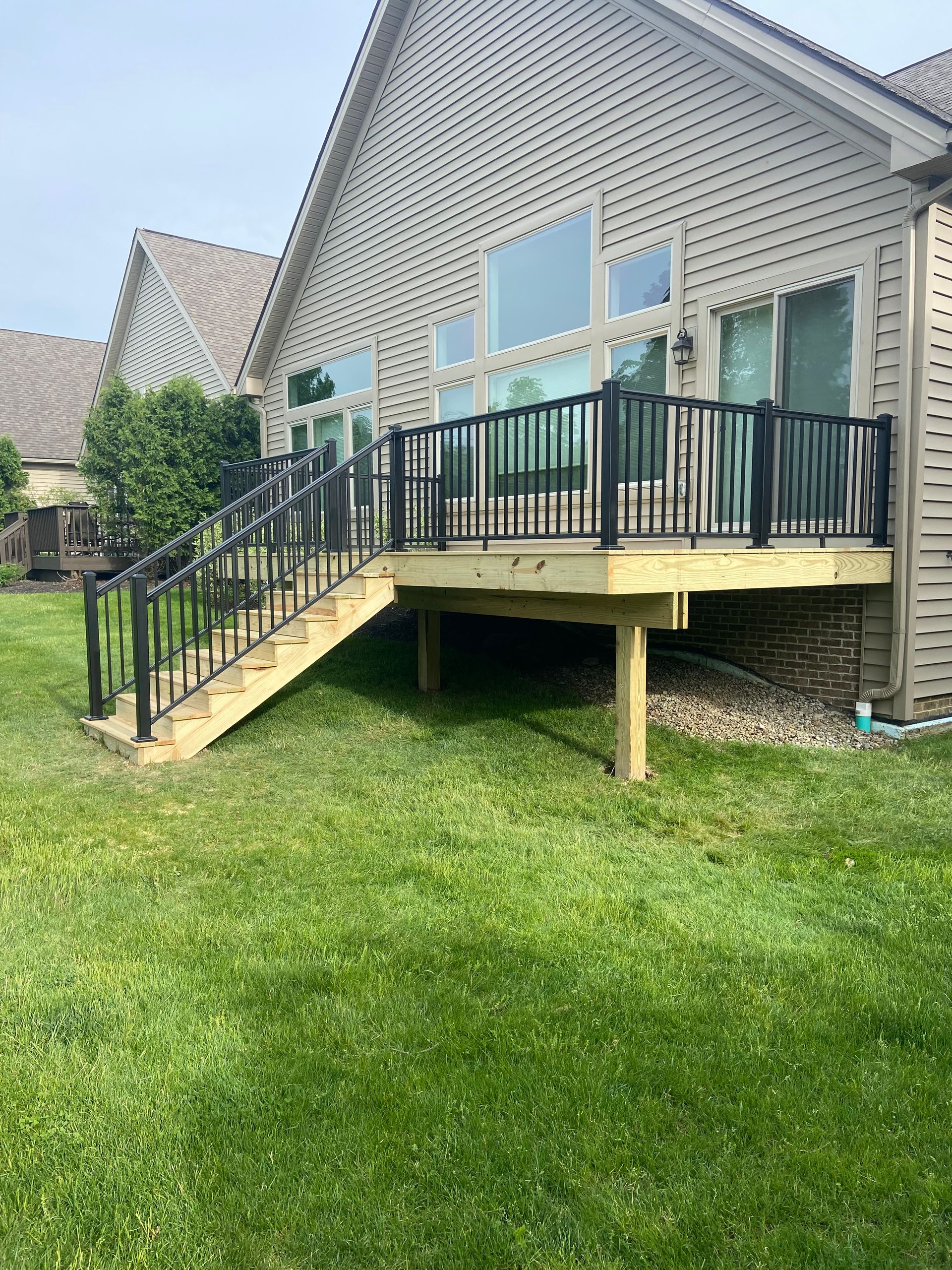 A wooden deck with black railings and stairs attached to a beige house, in a grassy yard.