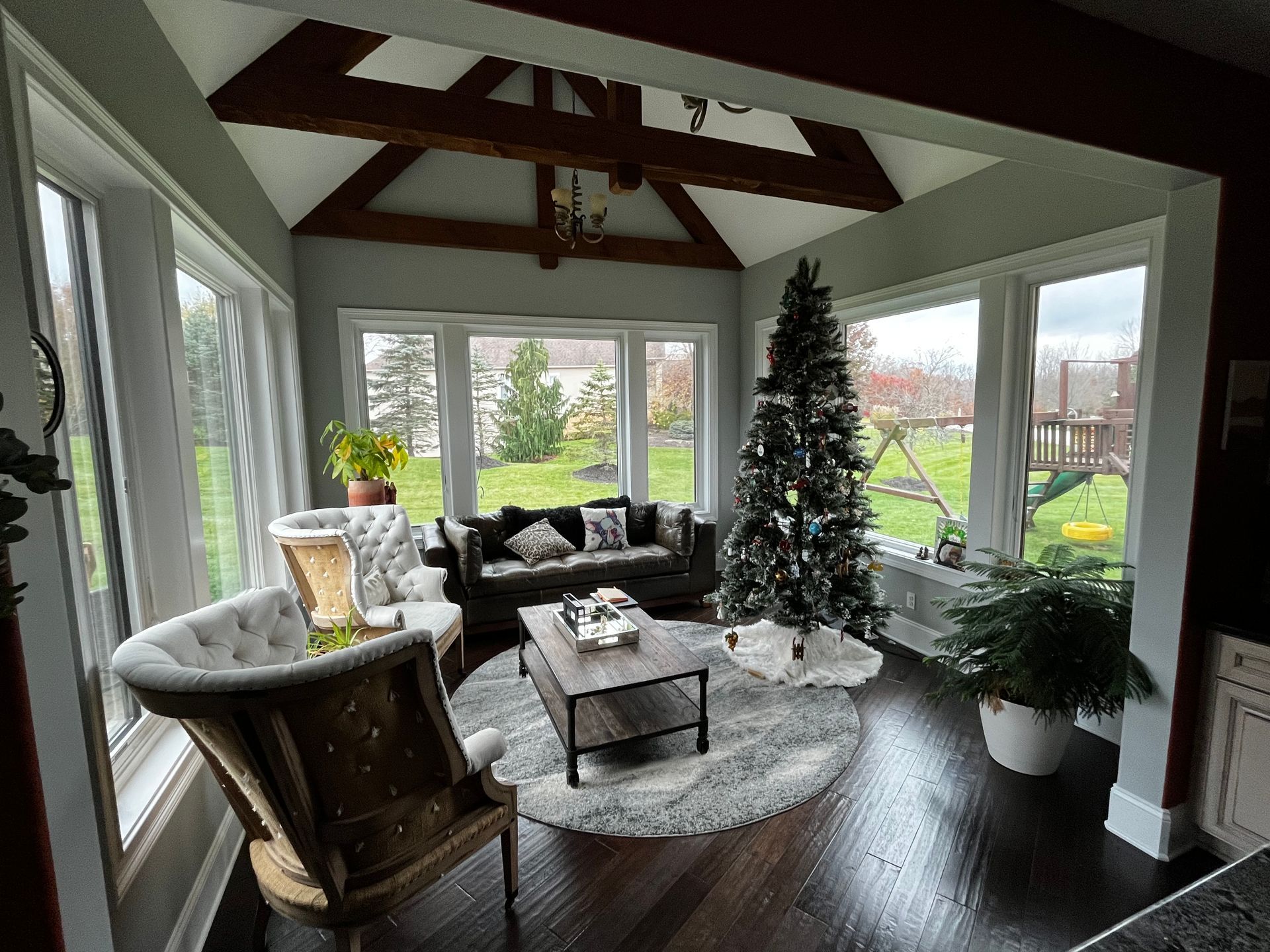 Sunroom with large windows, dark wood floors, seating, Christmas tree, and view of a yard.