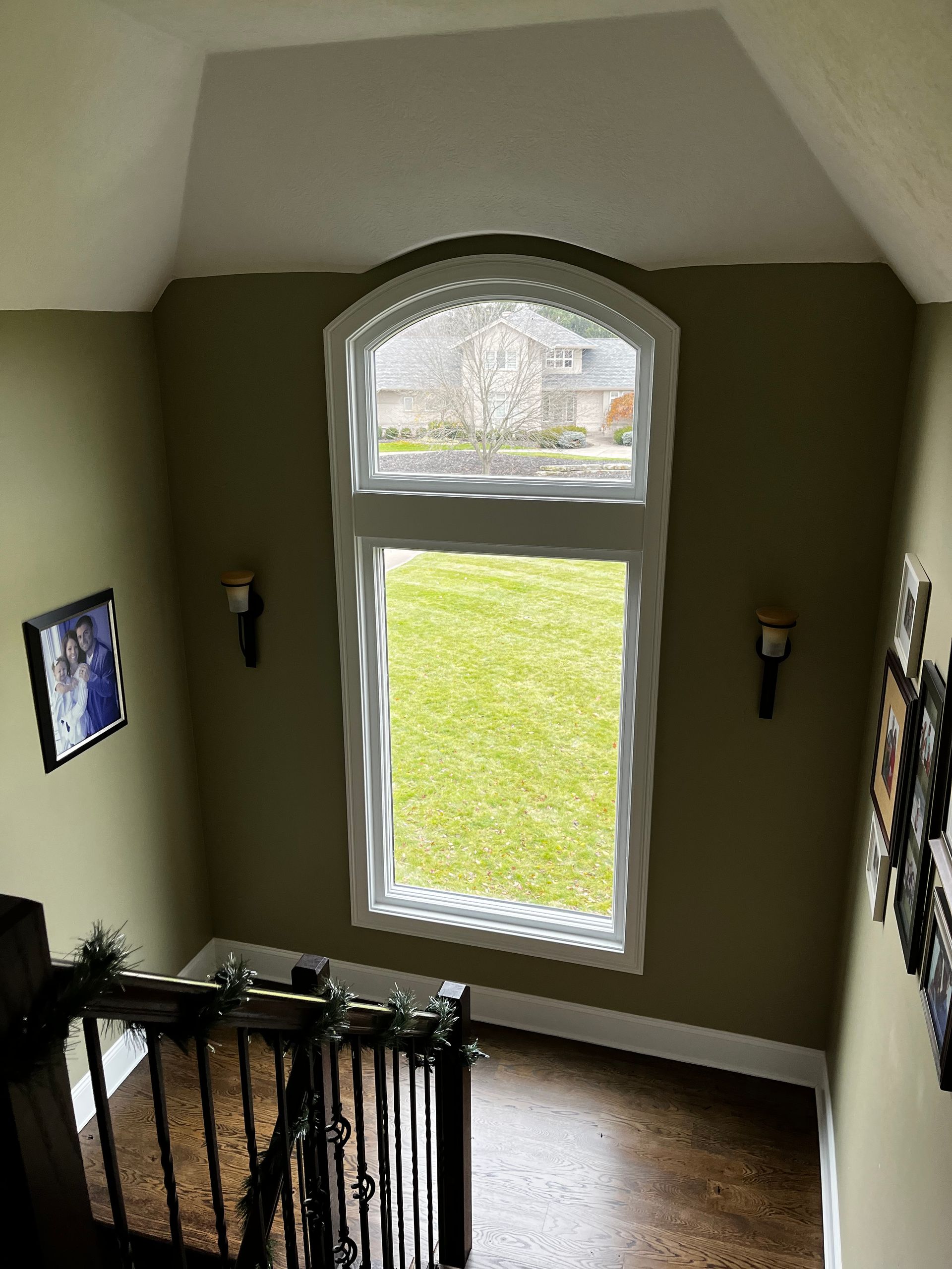 View from a staircase landing with a tall arched window overlooking a grassy yard; olive green walls.