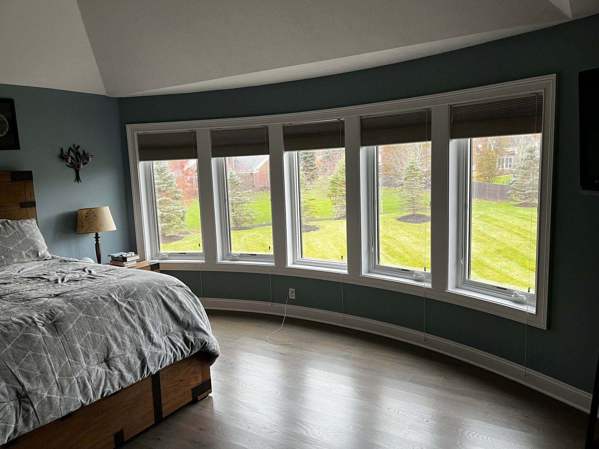 Bedroom with curved windows overlooking a yard, bed in the foreground, teal walls.