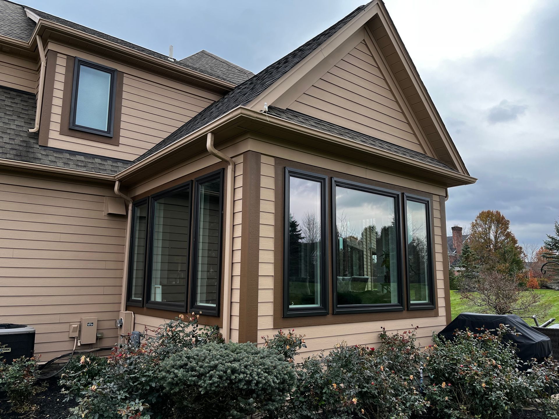 Beige house with dark-framed windows, brown trim, and a patterned roofline, cloudy day.