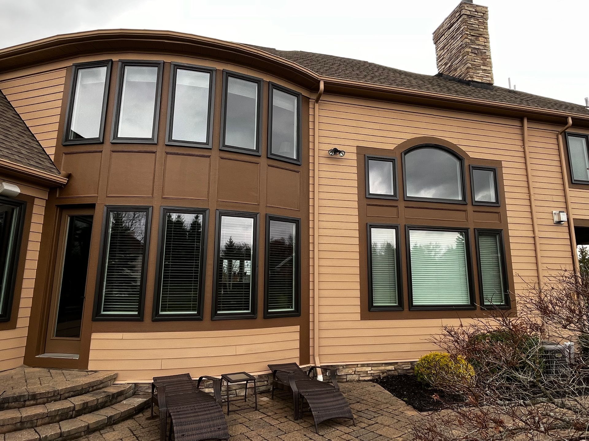 Tan house exterior with multiple windows, brown trim, and a brick chimney.