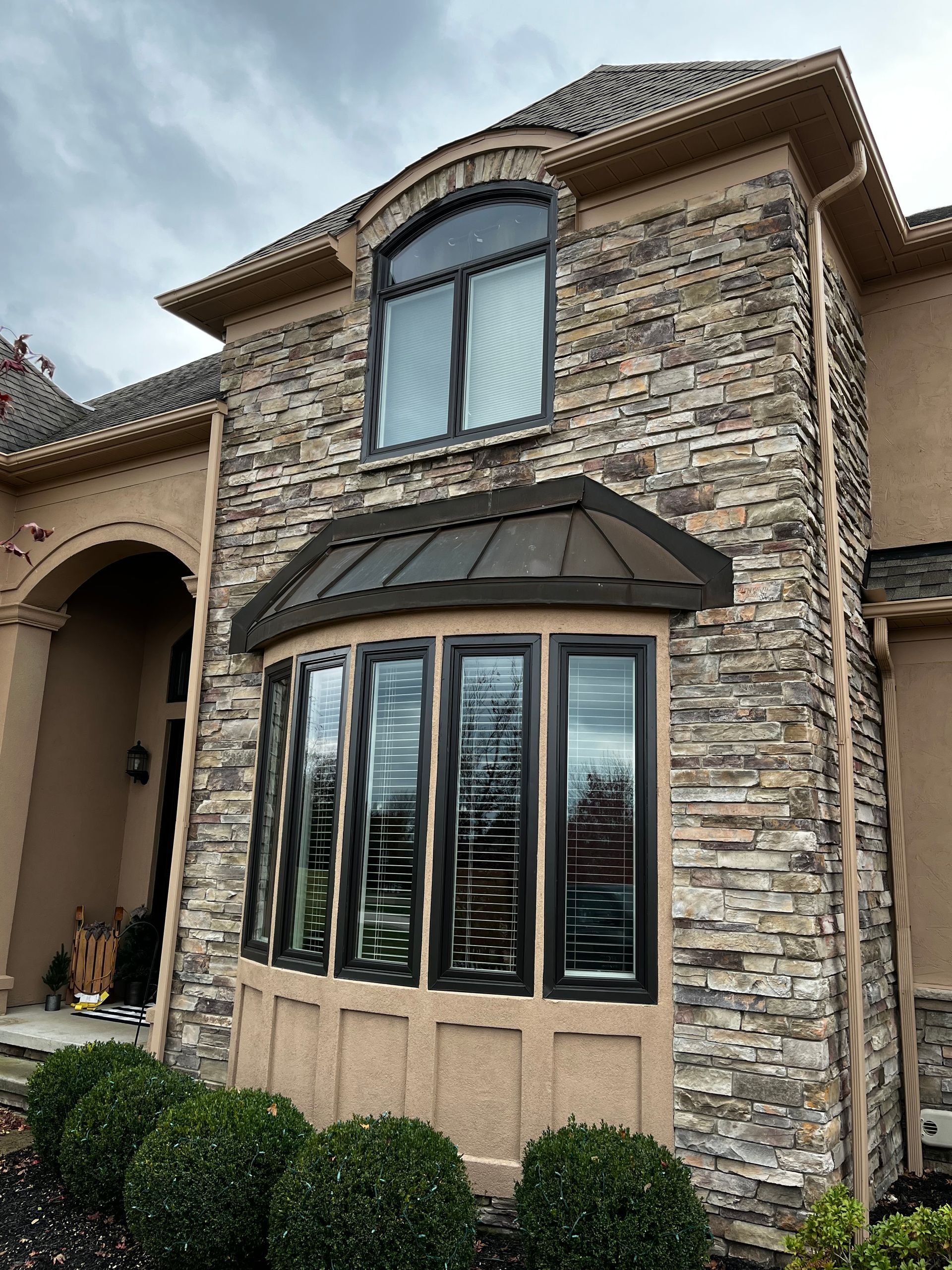 Tan house exterior with stone and tan trim, featuring arched and bay windows.