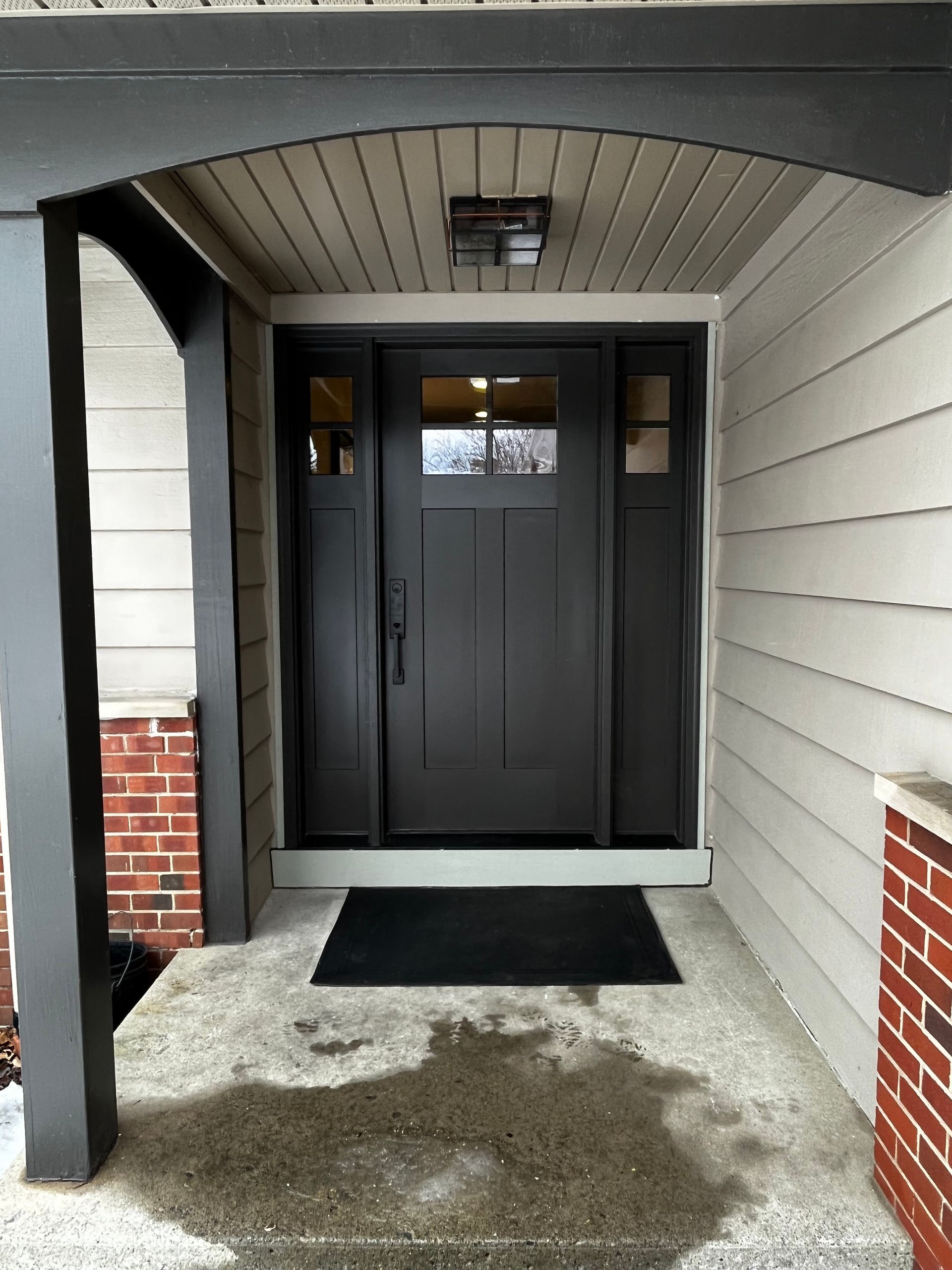 Black front door with sidelights under a covered porch.