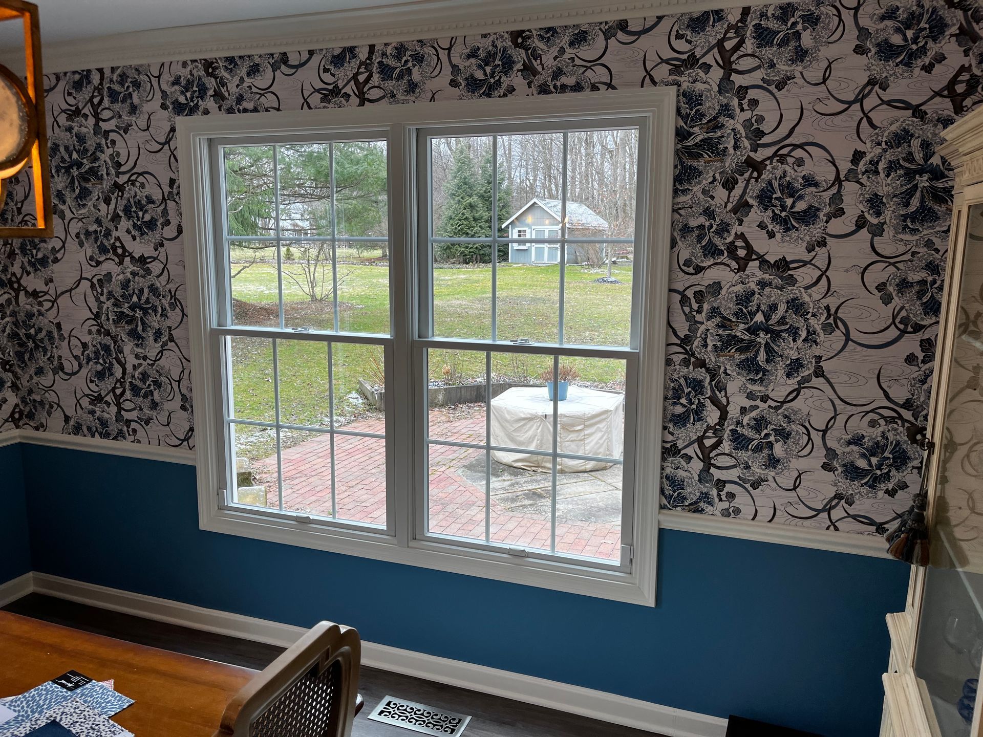 Interior dining room with blue and floral wallpaper, a window overlooking a yard.