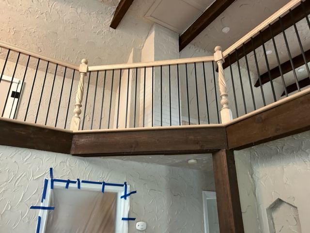Balcony with dark wood beams, white railings, and black spindles. Walls are textured and painted in neutral colors.