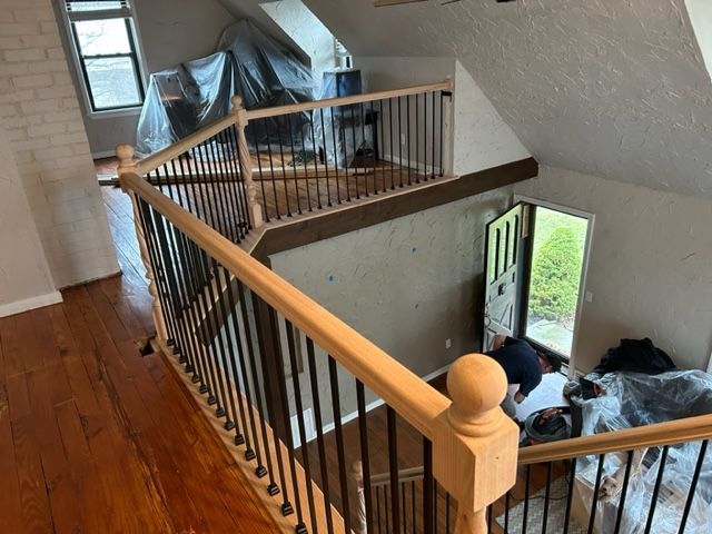 Interior view of a second-story landing with wood railings, black spindles, and an open door.