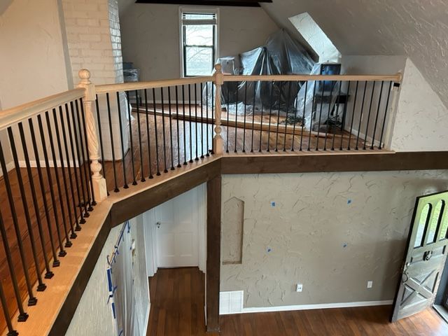Interior view of a renovated loft with hardwood floors, a railing with black spindles, and a window.
