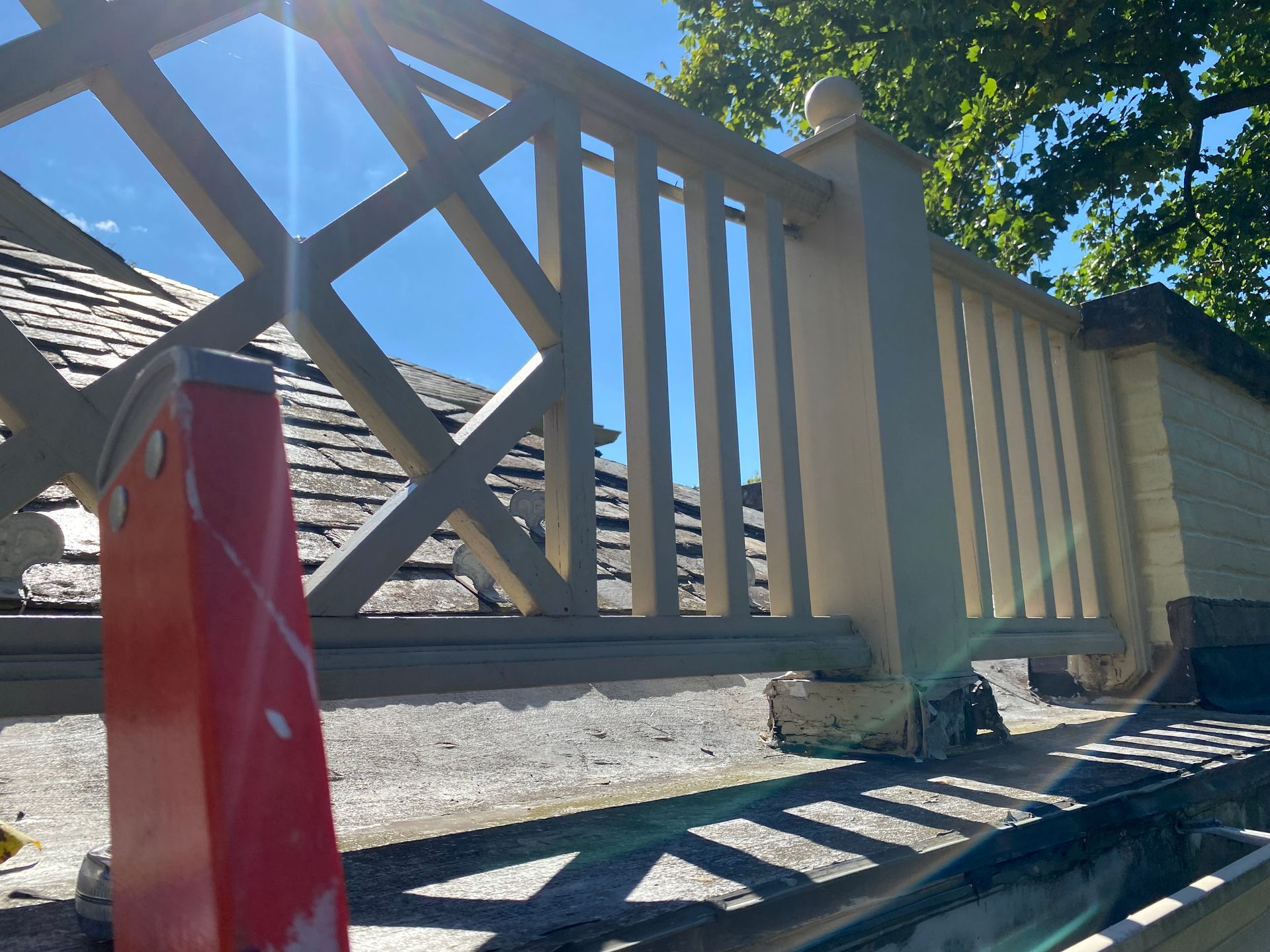 White and gray decorative wooden fence with a red object in front, against a roof and bright sky.