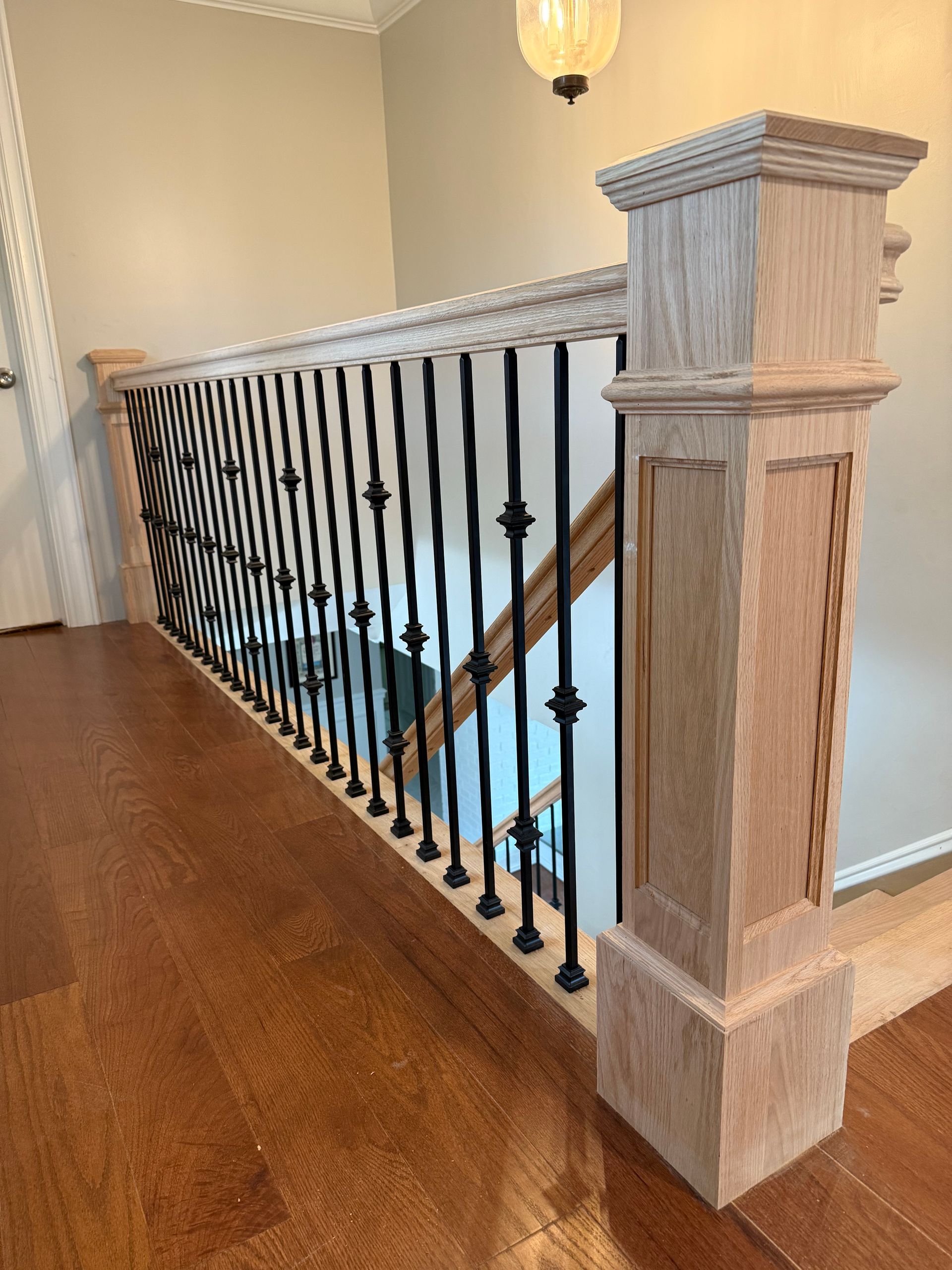 Wooden staircase with black iron spindles, light wood newel post, and brown hardwood floor.