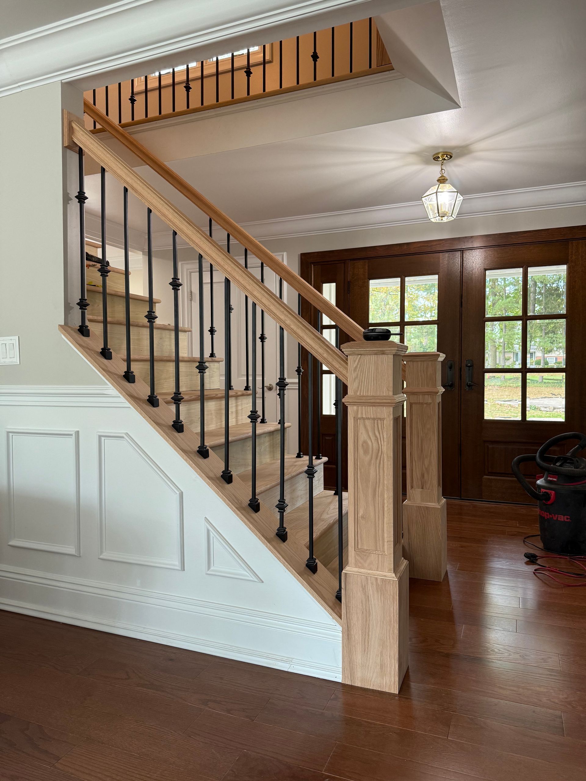 Staircase with light wood railings and black iron spindles, leading to upper level and entrance door.