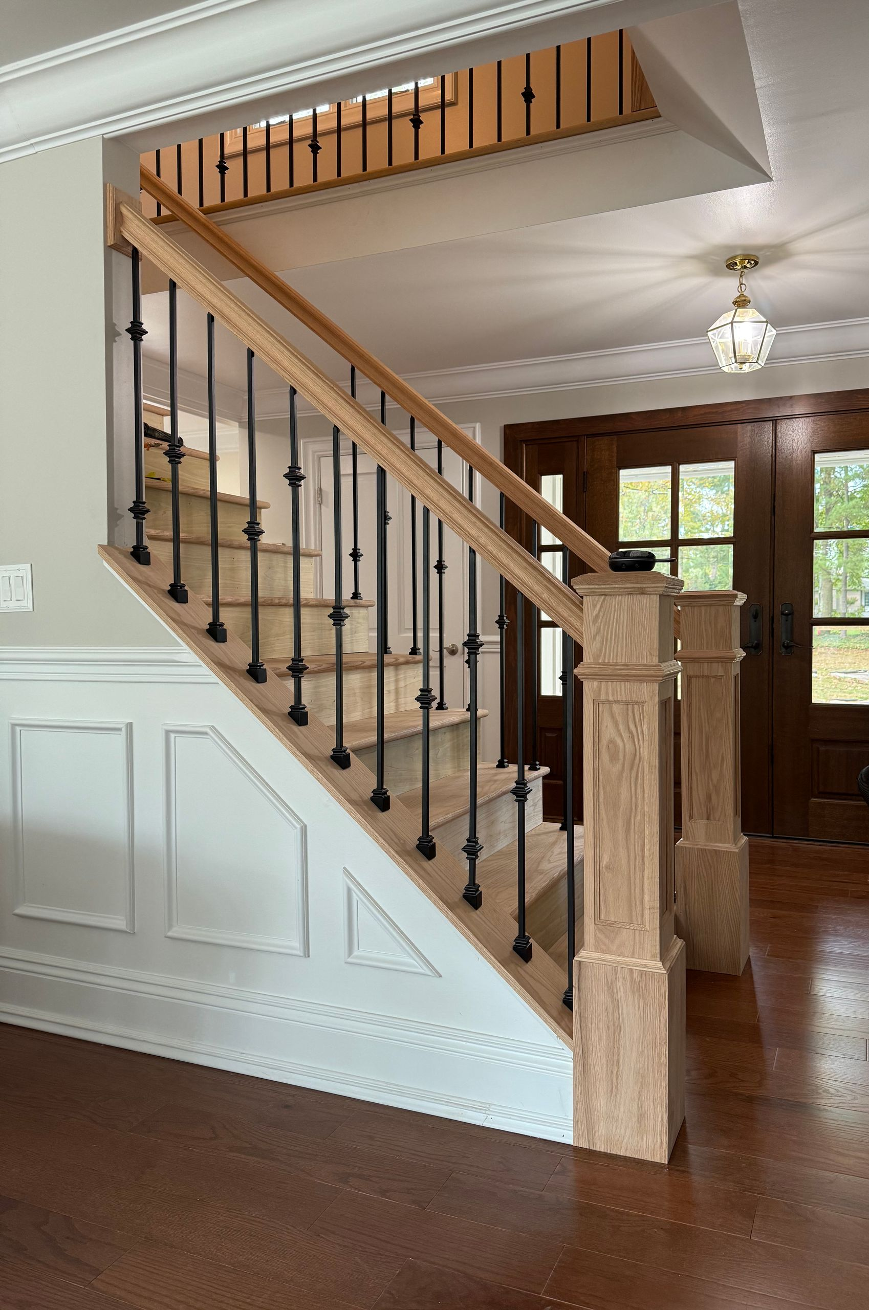 Staircase with light wood steps, black iron spindles, and detailed wood paneling.