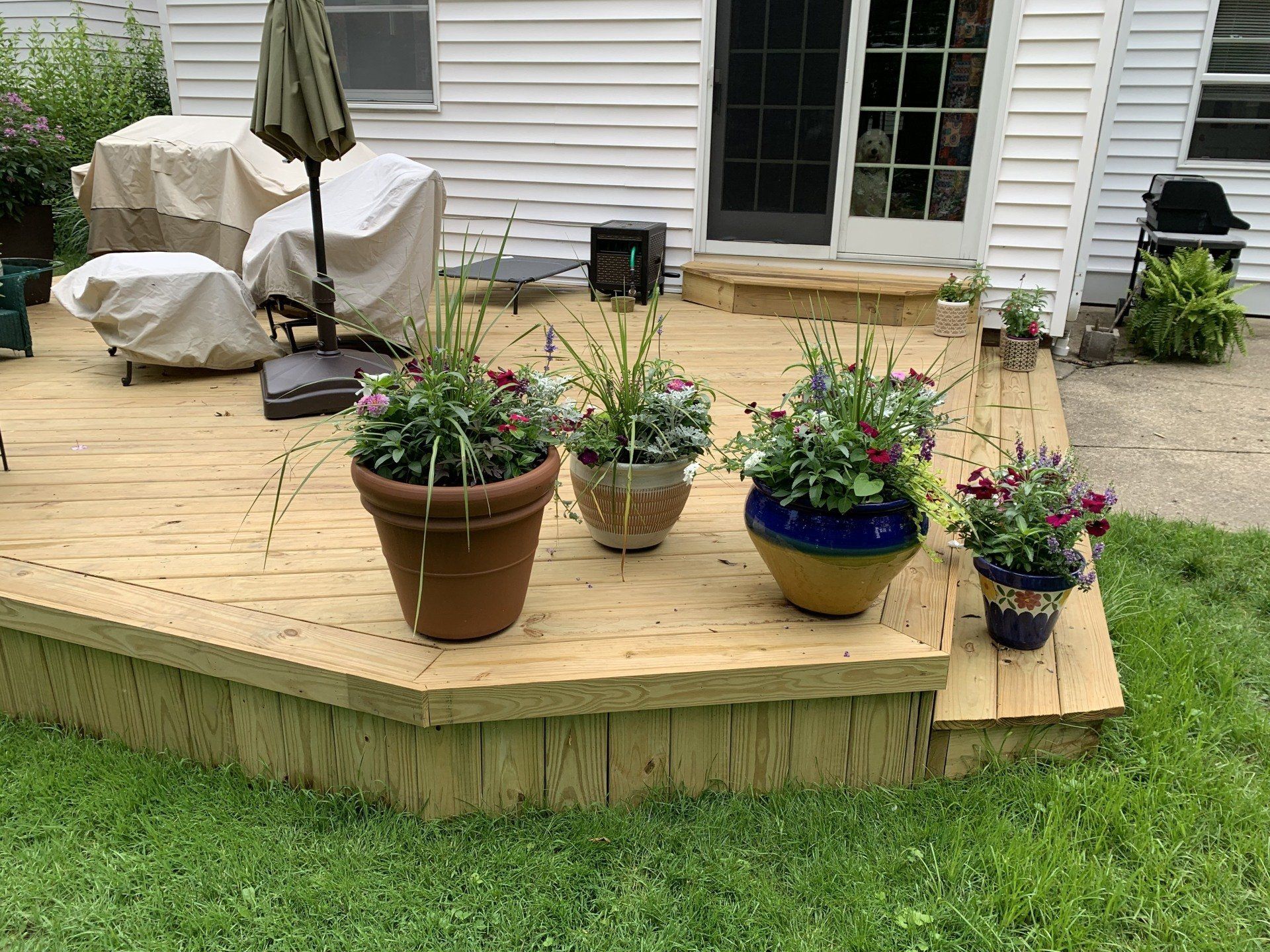 Wooden deck with potted flowers in front of a white house.