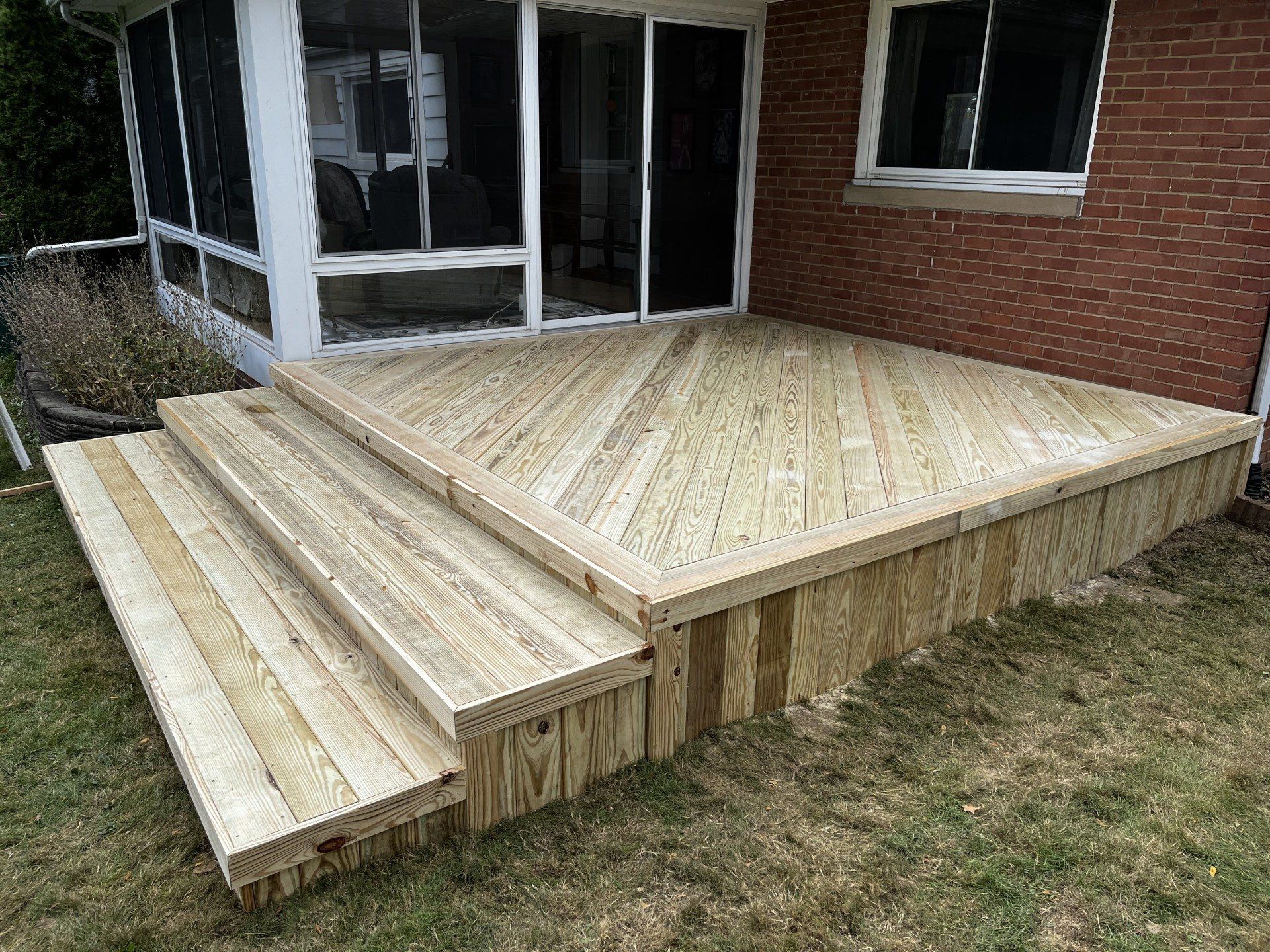 Wooden deck with steps next to a brick building and screened porch.