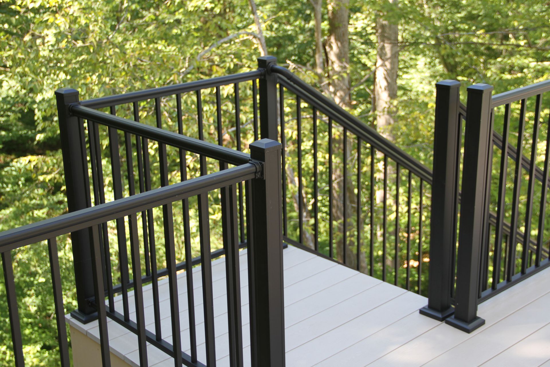 Black railing on a composite deck with stairs, surrounded by trees.