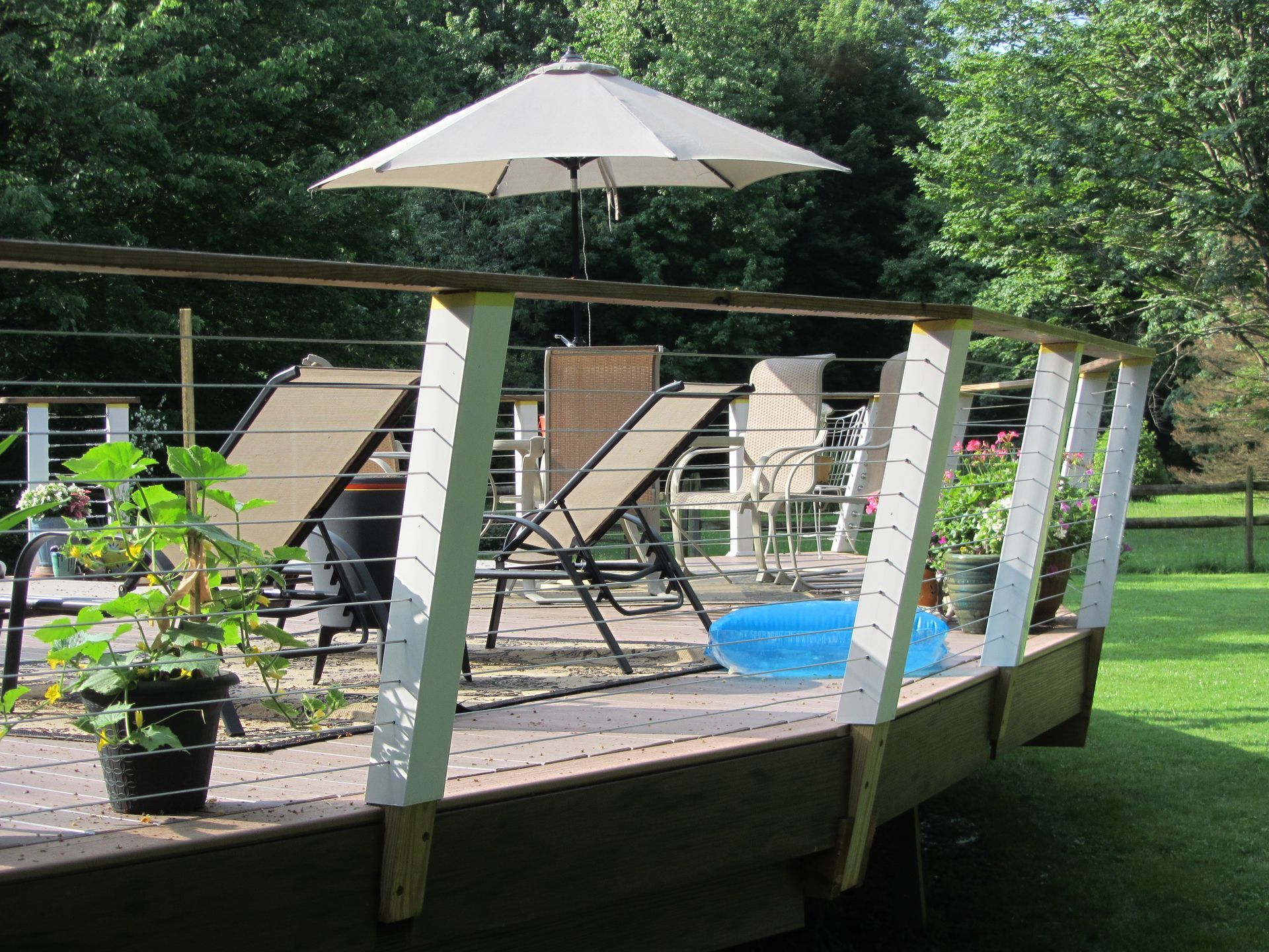 Deck with lounge chairs, umbrella, and potted plants in a backyard.